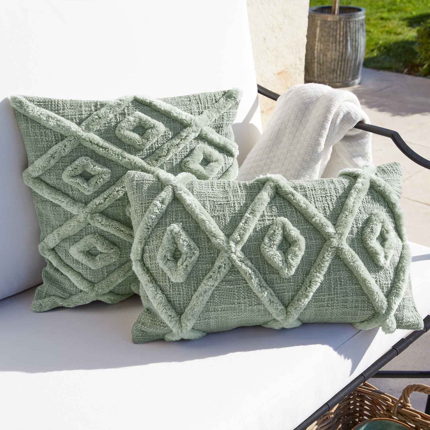 Weiches grünes Dekokissen mit geometrischem Muster auf weissem Gartenstuhl