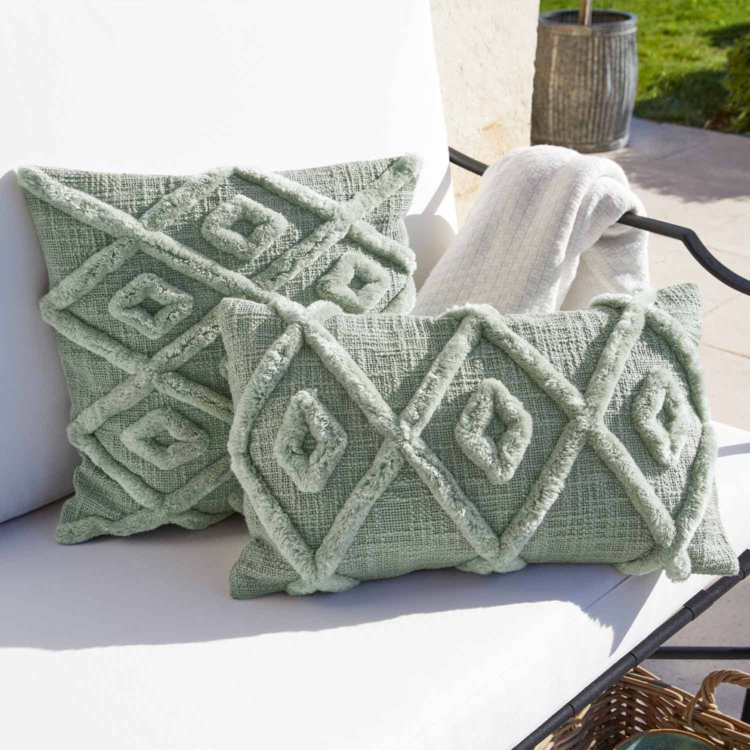 Weiches grünes Dekokissen mit geometrischem Muster auf weissem Gartenstuhl