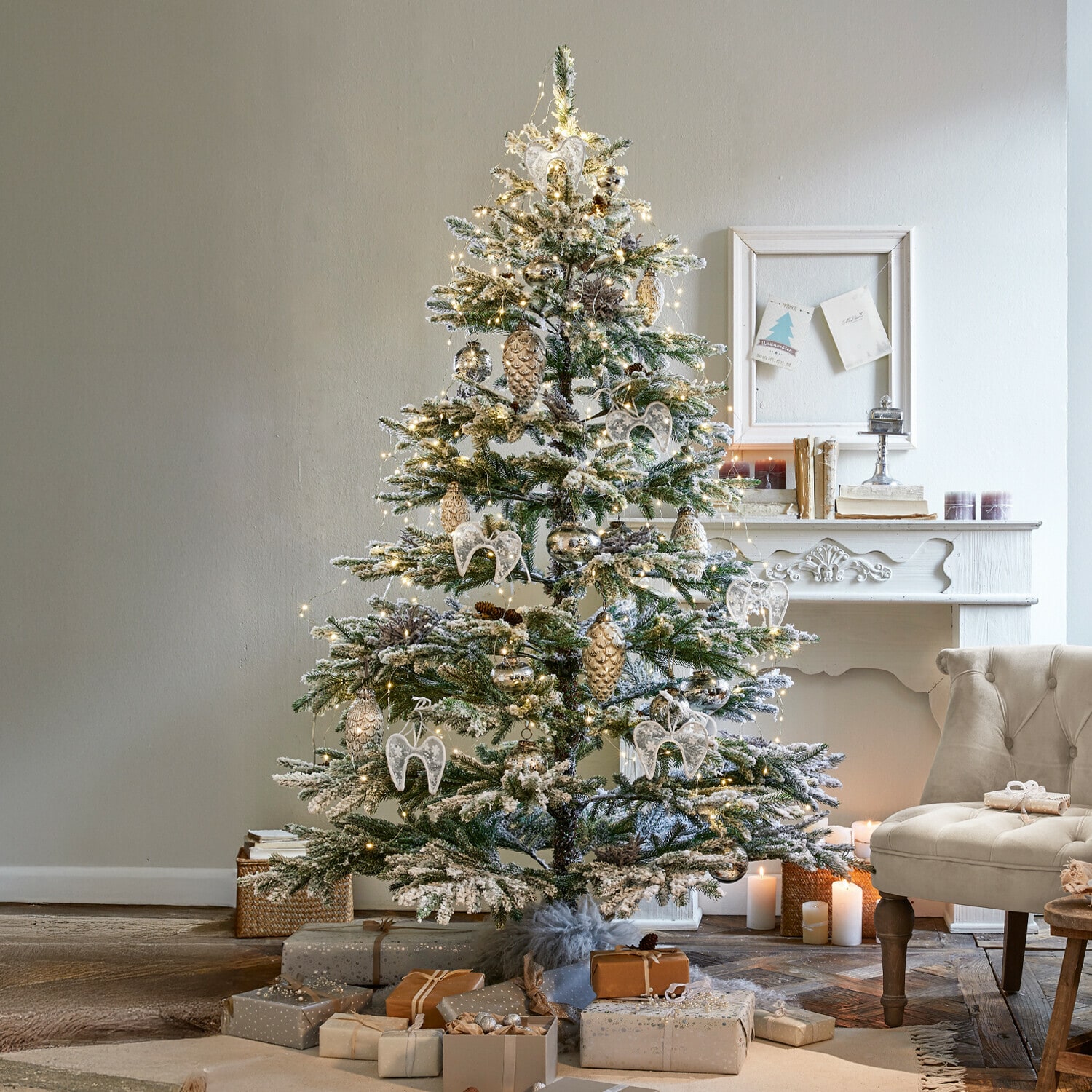 Weihnachtsbaum Lokossa Schneebedeckter Weihnachtsbaum mit weissen und goldenen Dekorationen und Geschenken neben einem beigen Sessel im gemütlichen Wohnzimmer