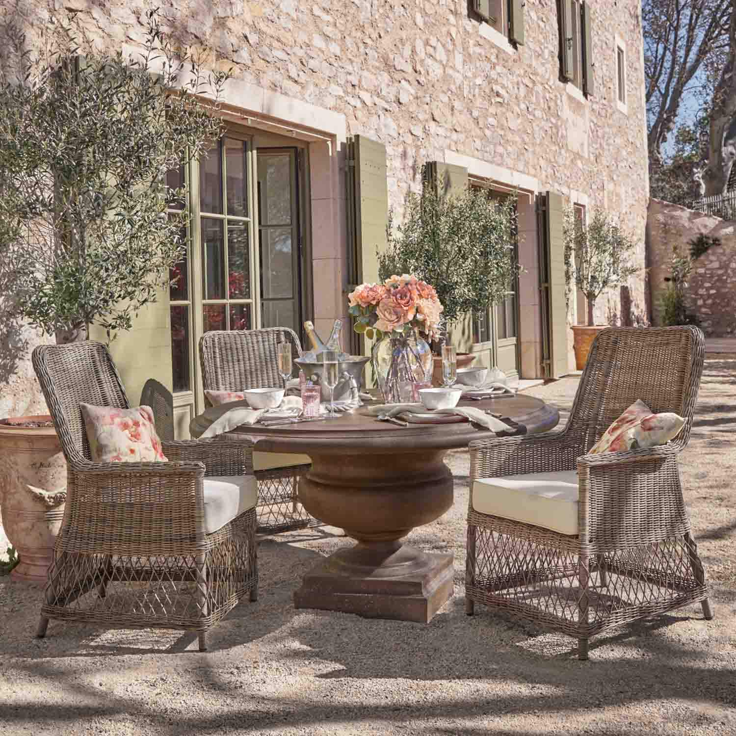 Runder Steintisch mit Rattanstühlen und Blumenarrangement auf sonniger Gartenterrasse