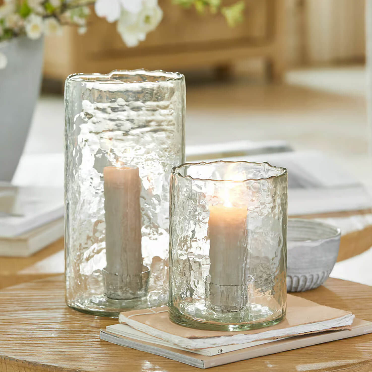 Zwei durchsichtige Glaswindlichter mit weissen Kerzen auf Holztisch, stilvolle Wohnraumdekoration