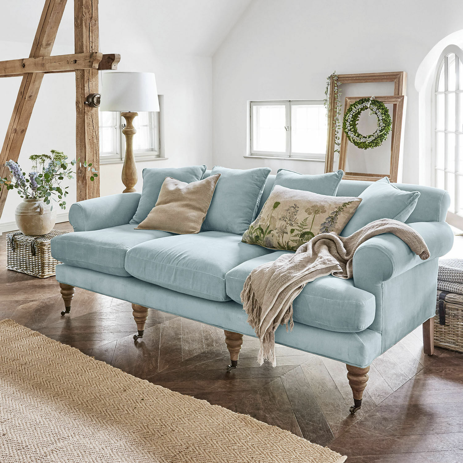 Sofa Kazimir Hellblaues Sofa aus Stoff mit Kissen und Decke in einem gemütlichen, hellen Wohnzimmer