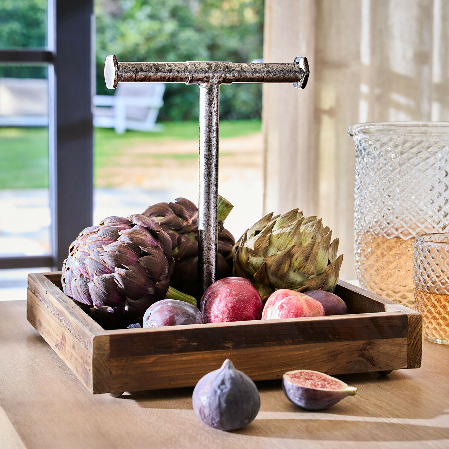 Holztablett mit Metallgriff gefüllt mit Artischocken und Pflaumen auf hellem Tisch im Raum