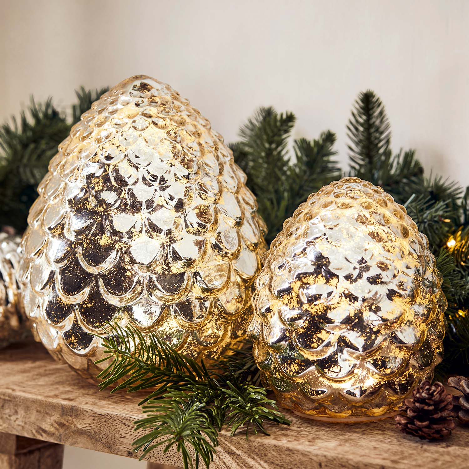 Goldene Glasdekorationen in Zapfenform auf Holzregal mit grünen Tannenzweigen