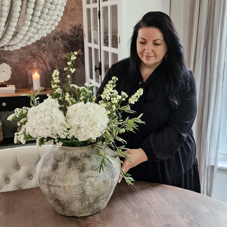 Grosse graue Keramikvase mit weissen Blumen auf Holztisch in gemütlichem Raum