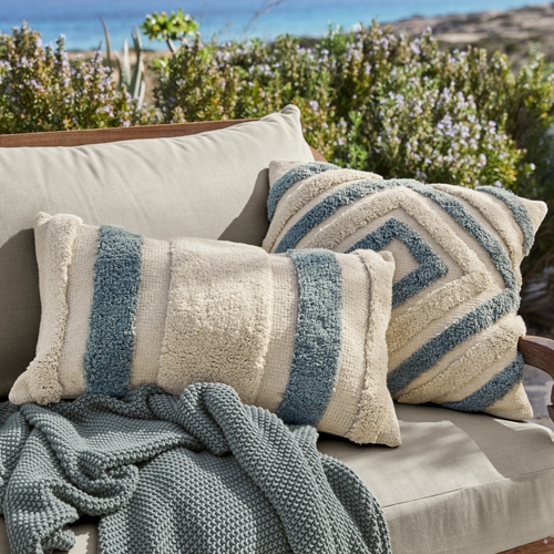 Beige-blaue dekorative Kissen aus weichem Material auf grauem Sofa im Aussenbereich, Gartentextilien