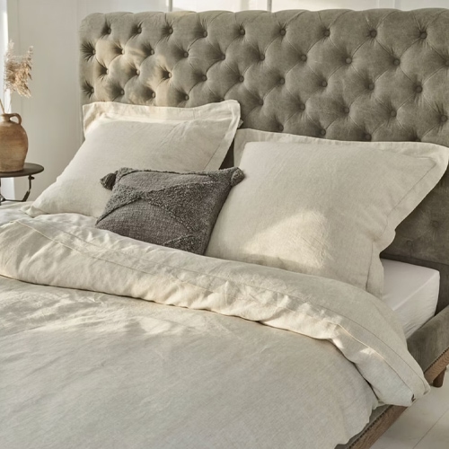 Beige Leinenbettwäsche auf Bett mit grauem, gesteppterem Kopfteil, natürliche Stoffe fürs Schlafzimmer