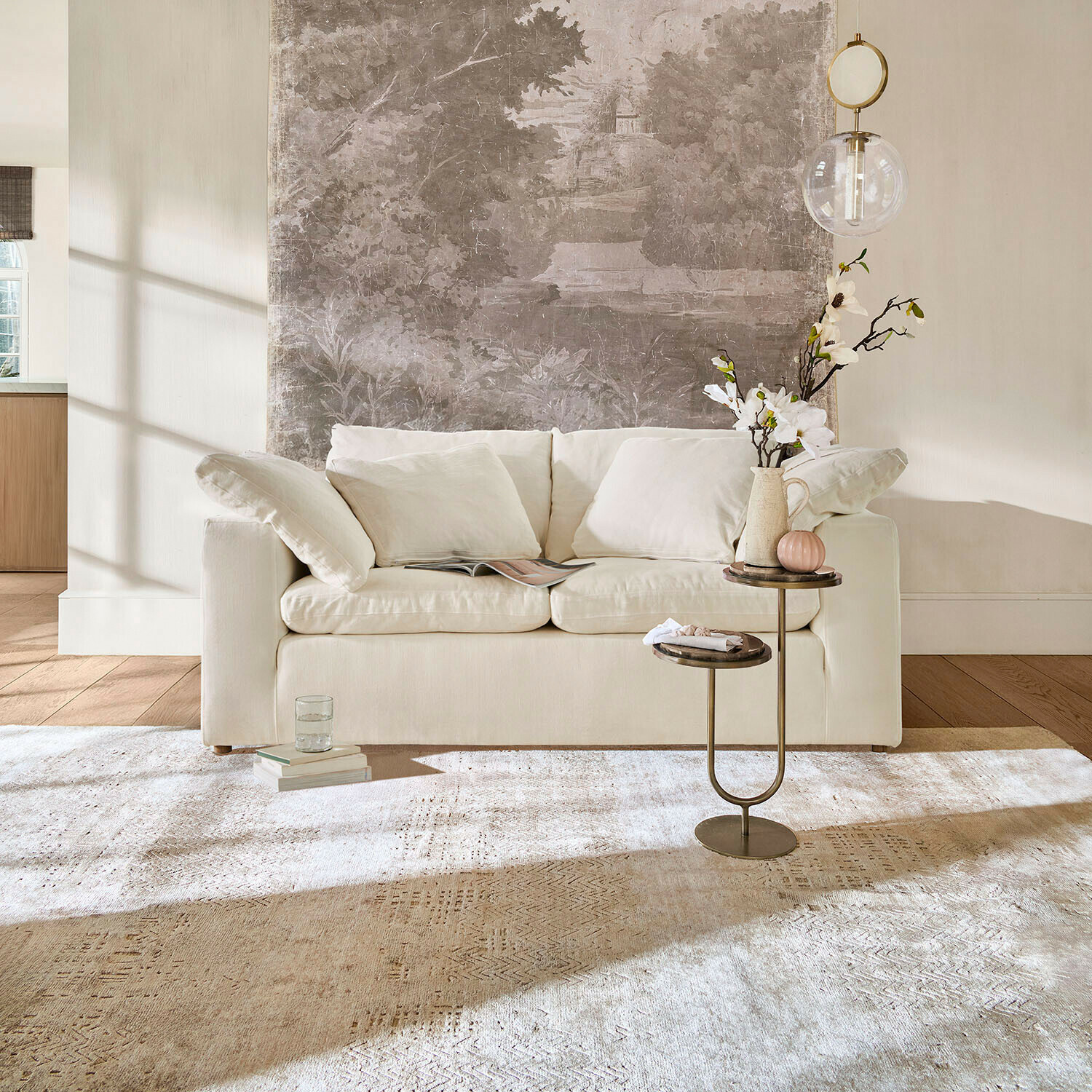 Beige Sofa mit weichen Kissen vor Wand mit dekorativem Wandbild und Beistelltisch mit Blumen