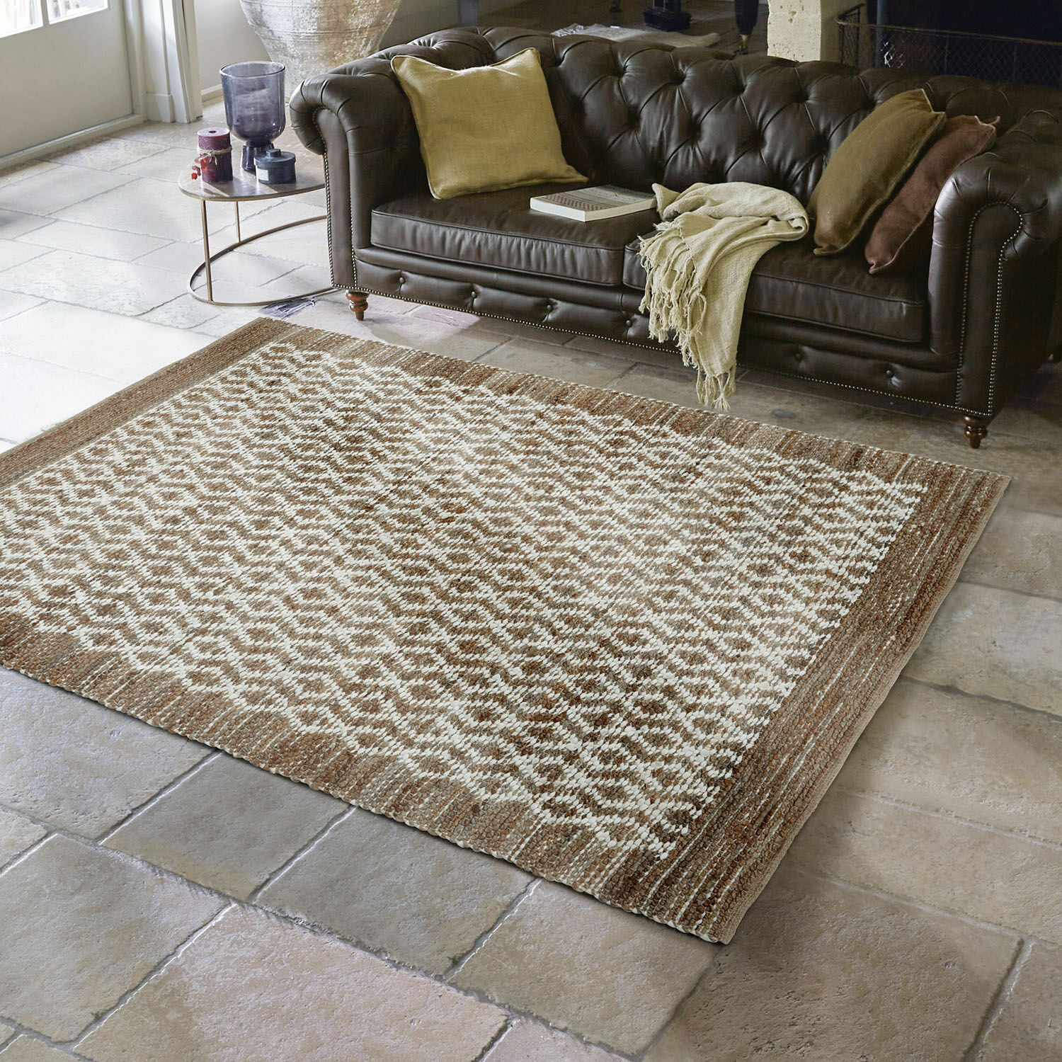Wendeteppich Amhara Braun-beiger Teppich mit geometrischem Muster auf Steinboden vor dunkelbraunem Ledersofa im Wohnzimmer