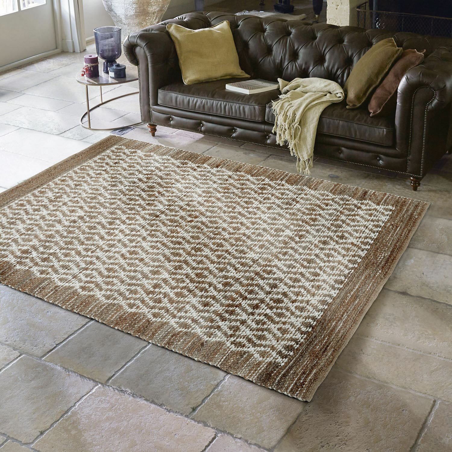 Wendeteppich Amhara Braun-beiger Teppich mit geometrischem Muster auf Steinboden vor dunkelbraunem Ledersofa im Wohnzimmer