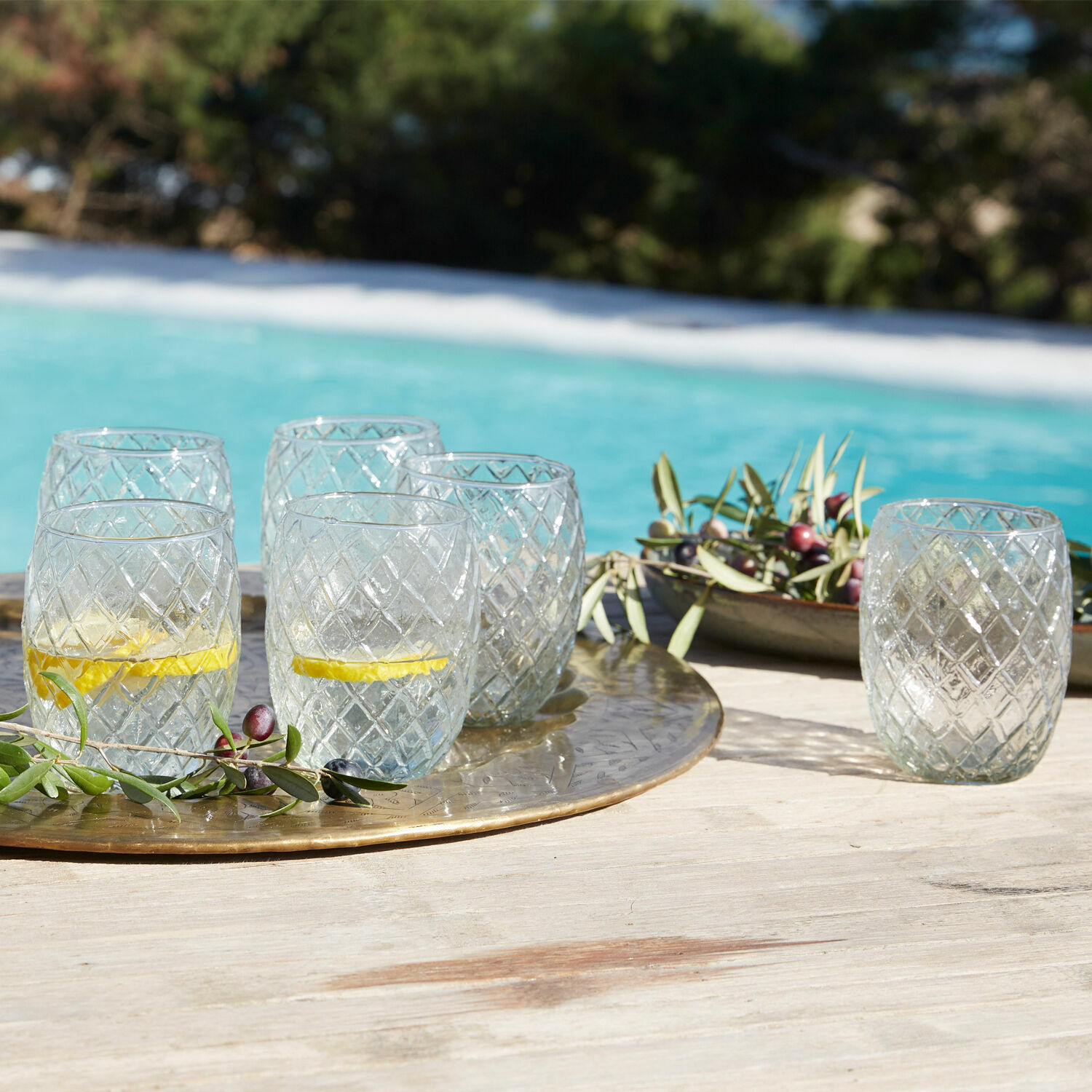 Glas 6er Set Corrofin Gläser aus klarem Glas mit Diamantmuster auf goldfarbenem Tablett am Poolrand