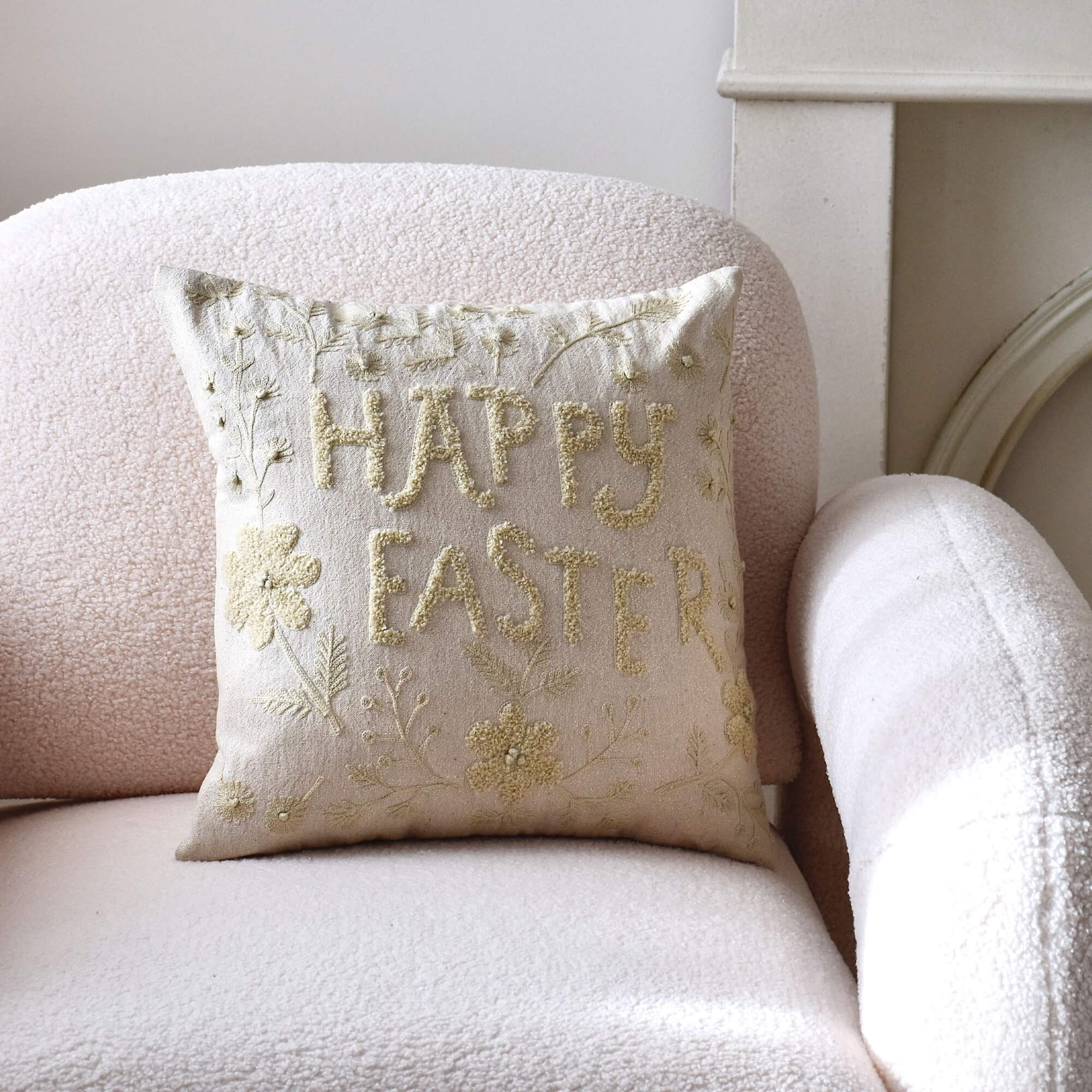 Beige Dekokissen mit Stickerei «Happy Easter» auf hellem Sessel, pastellfarbenes Osterdesign