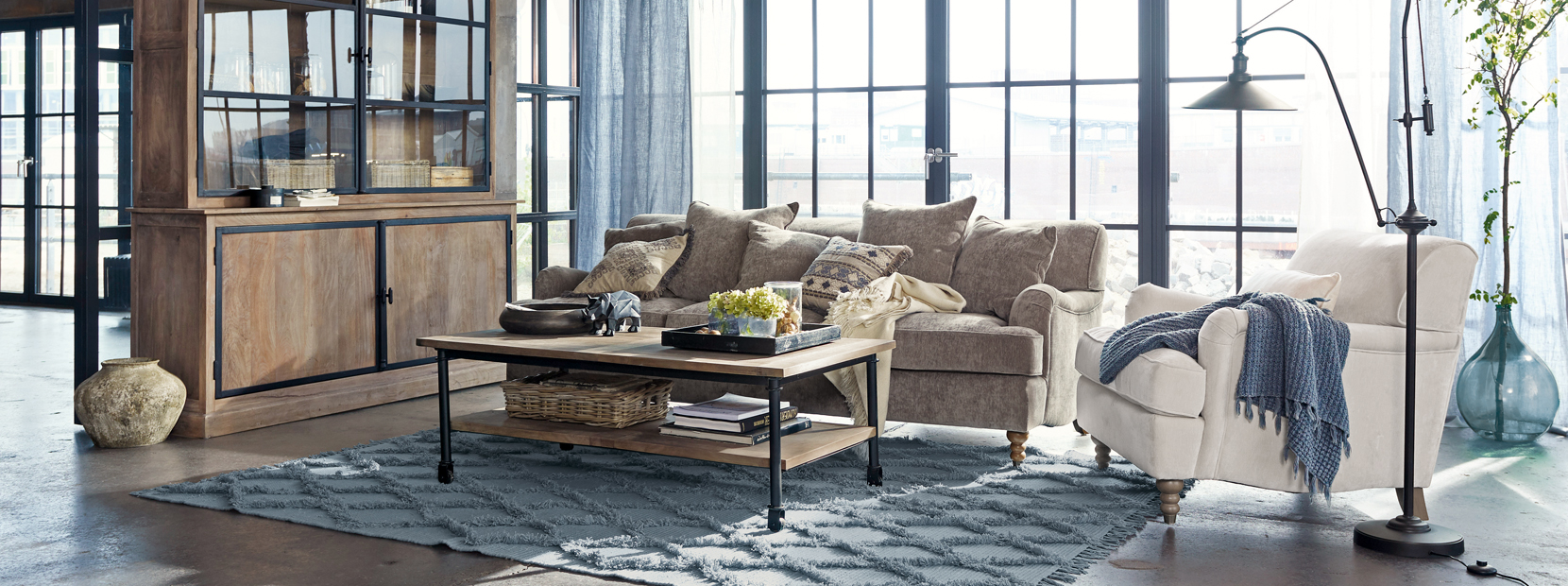 Industrielles Wohnzimmer mit Holzschrank, grauem Sofa und beigem Sessel auf blauem Teppichboden