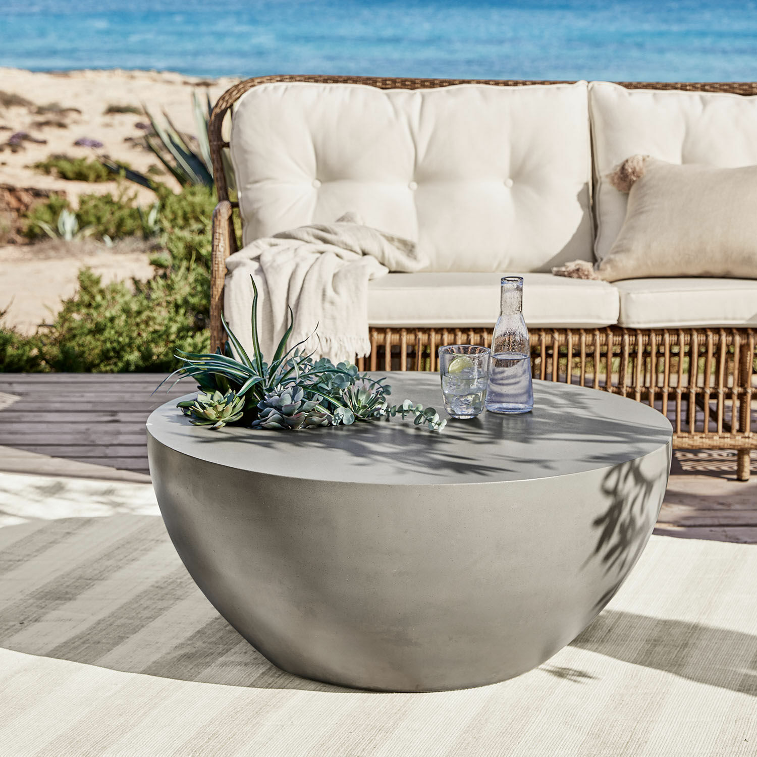 Couchtisch Plévin Runder grauer Couchtisch aus Beton auf der Terrasse mit Sukkulenten-Dekoration und Wasserglas