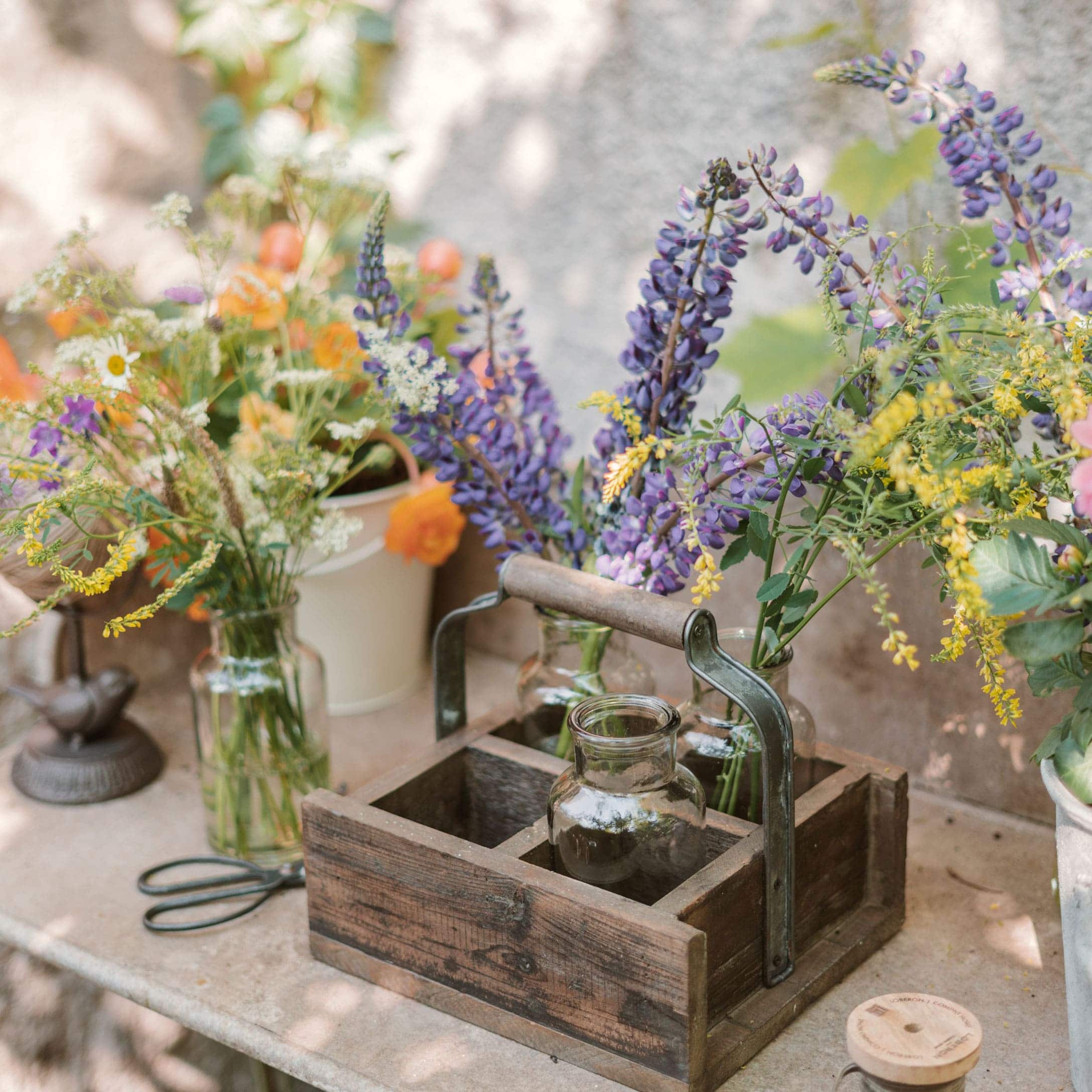 Holz-Organizer mit Griff und Glasvasen mit bunten Blumen auf einem Gartentisch