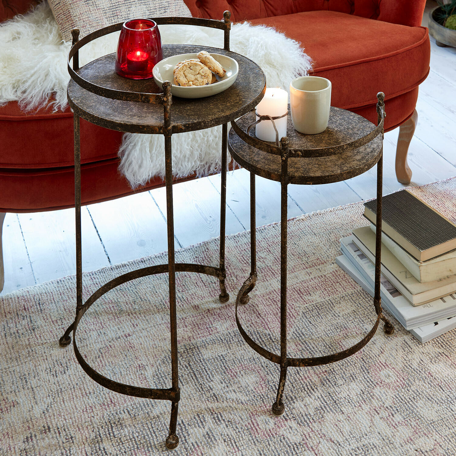 Beistelltisch 2er Set Alanyn Zwei runde Beistelltische aus Metall mit antikem Bronze-Finish auf Teppich vor rotem Sofa