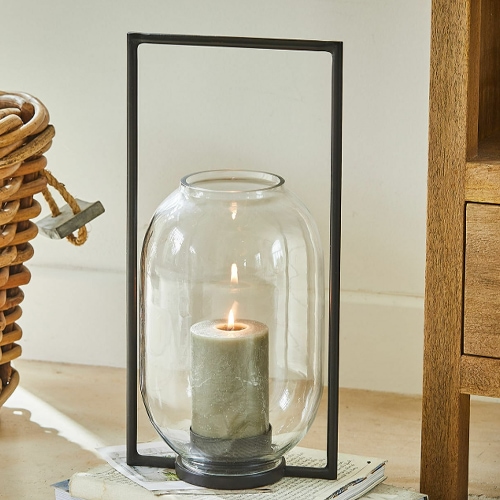 Glaslaterne mit schwarzem Metallrahmen und grüner Kerze als Wohnaccessoire
