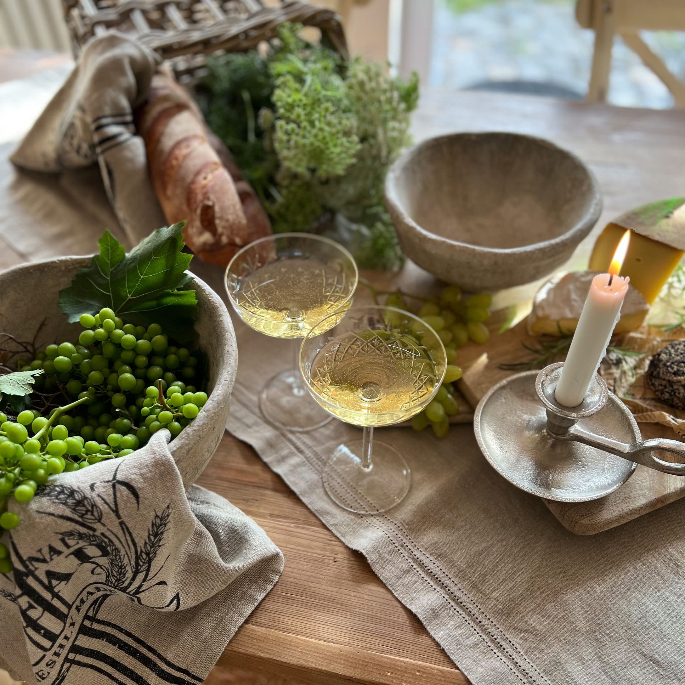 Rustikaler Holztisch mit Steinschalen, brennender Kerze, Weissweingläsern, Brot und grünen Trauben