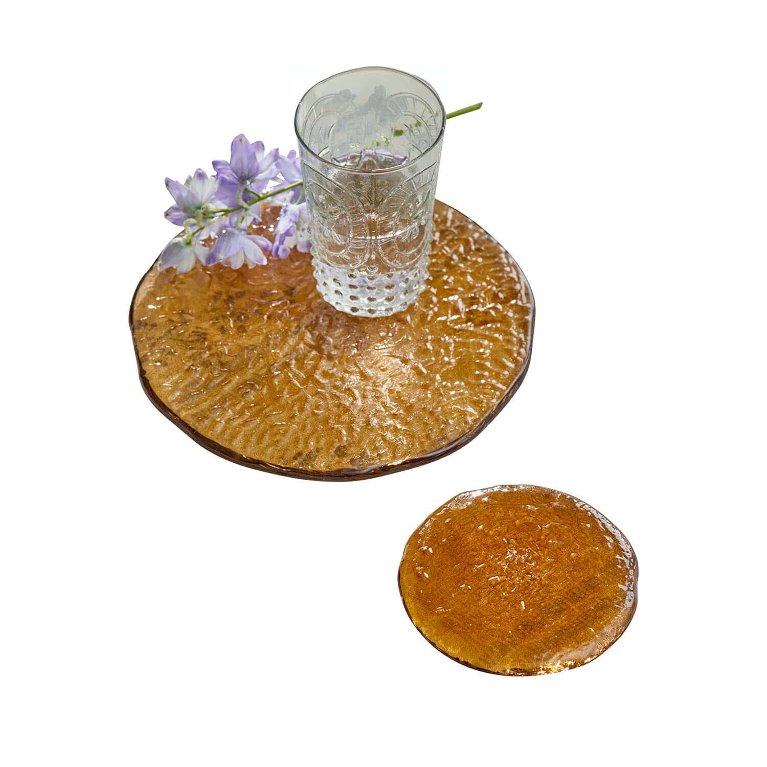 Transparenter Glasbecher auf strukturierter bernsteinfarbener Glasunterlage mit lila Blume