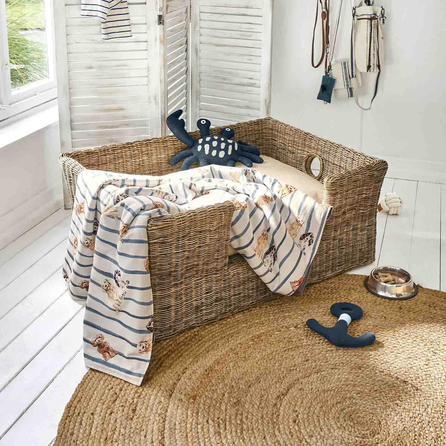 Geflochtenes Hundebett mit beigem Kissen, gestreifter Decke mit Hunde-Motiv, Spielzeug und Napf