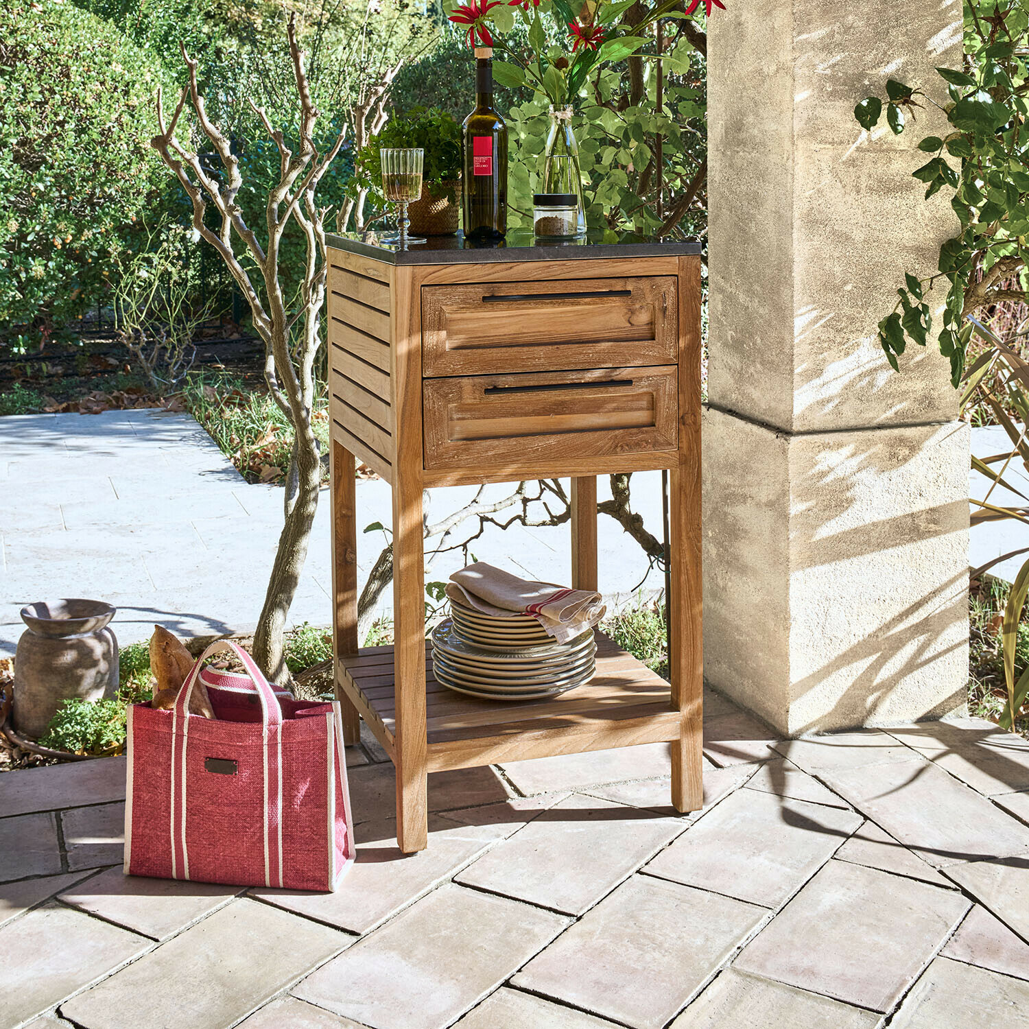 Holzkommode mit schwarzer Platte und zwei Schubladen auf Terrasse mit Geschirr und Weinflasche