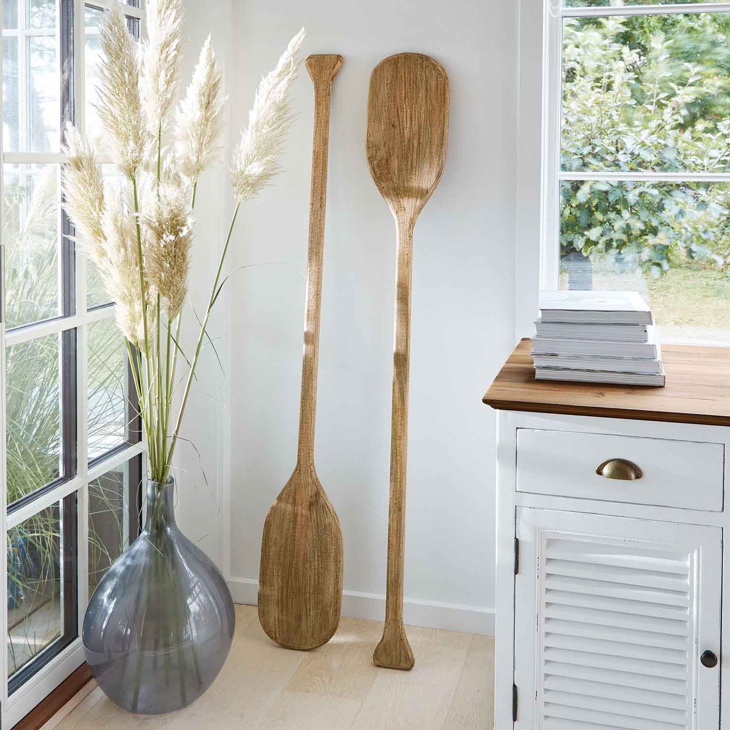 Zwei dekorative Paddel aus Holz in Naturfarbe lehnen an weisser Wand in hellem Raum