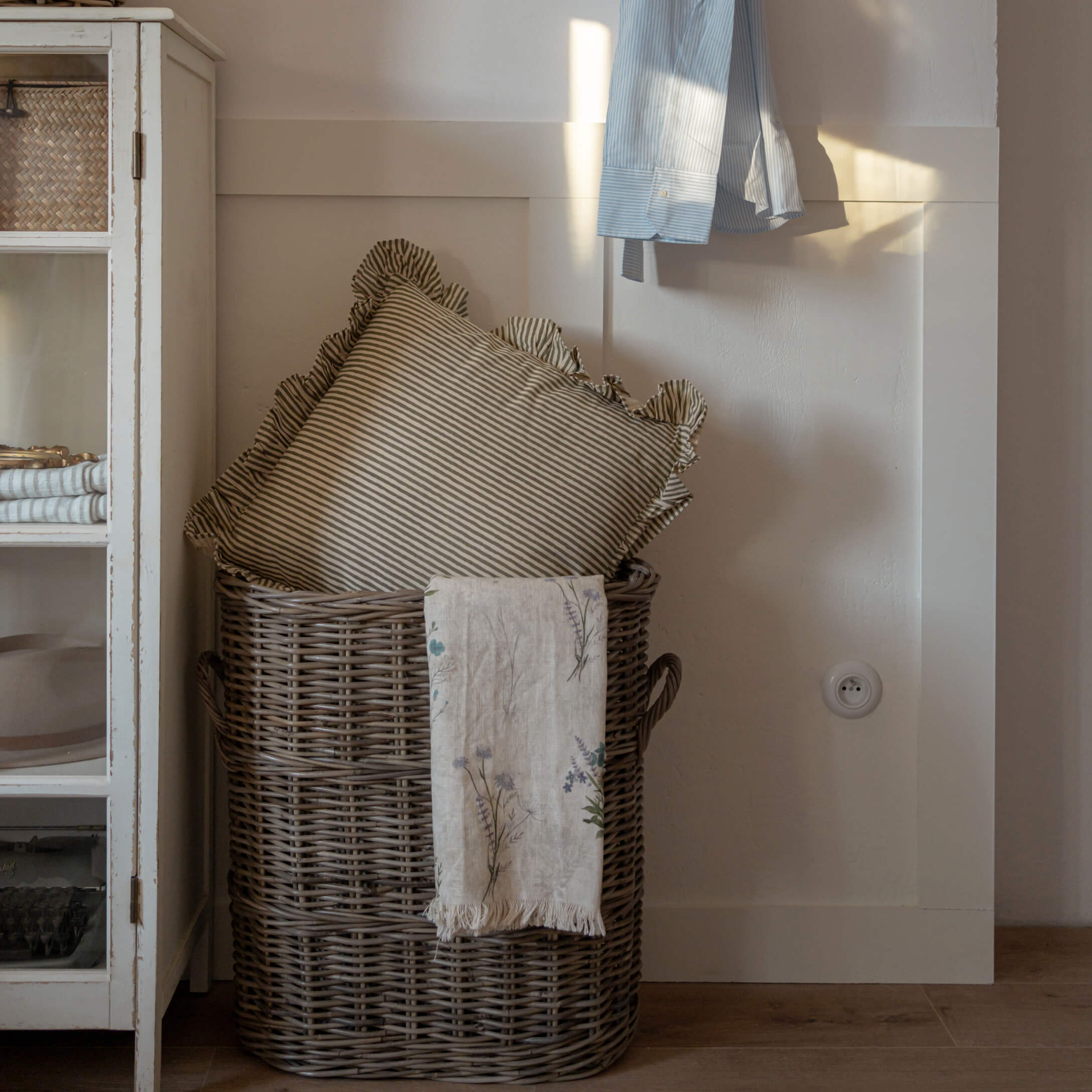 Brauner Weidenkorb mit gestreiftem Kissen und Leinen-Decke mit Blumenmuster in gemütlichem Raum