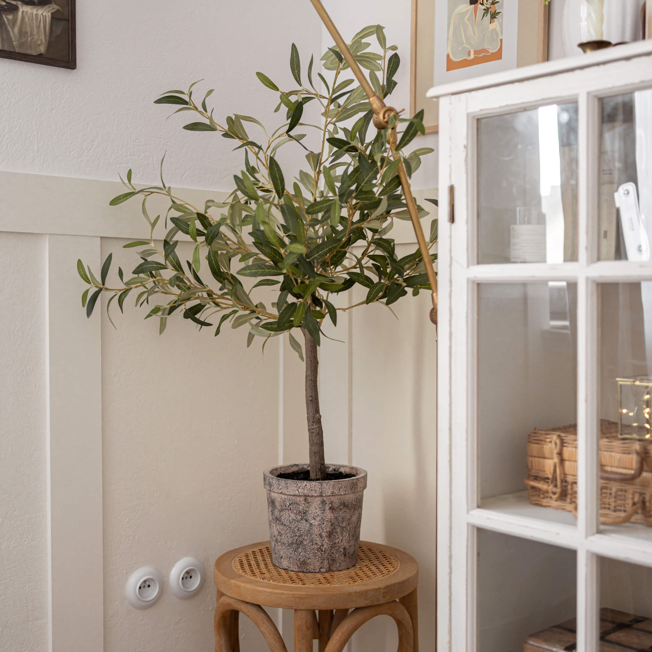 Künstlicher Olivenbaum in Steintopf auf Holzschemel in hellem Raum