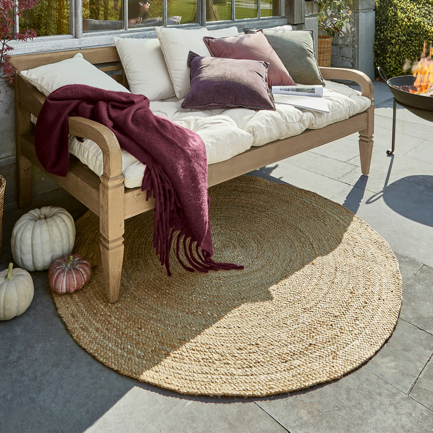Teppich Imene Runder Jute-Teppich in Naturfarbe unter einer Holzbank mit Kissen und bordeauxroter Wolldecke