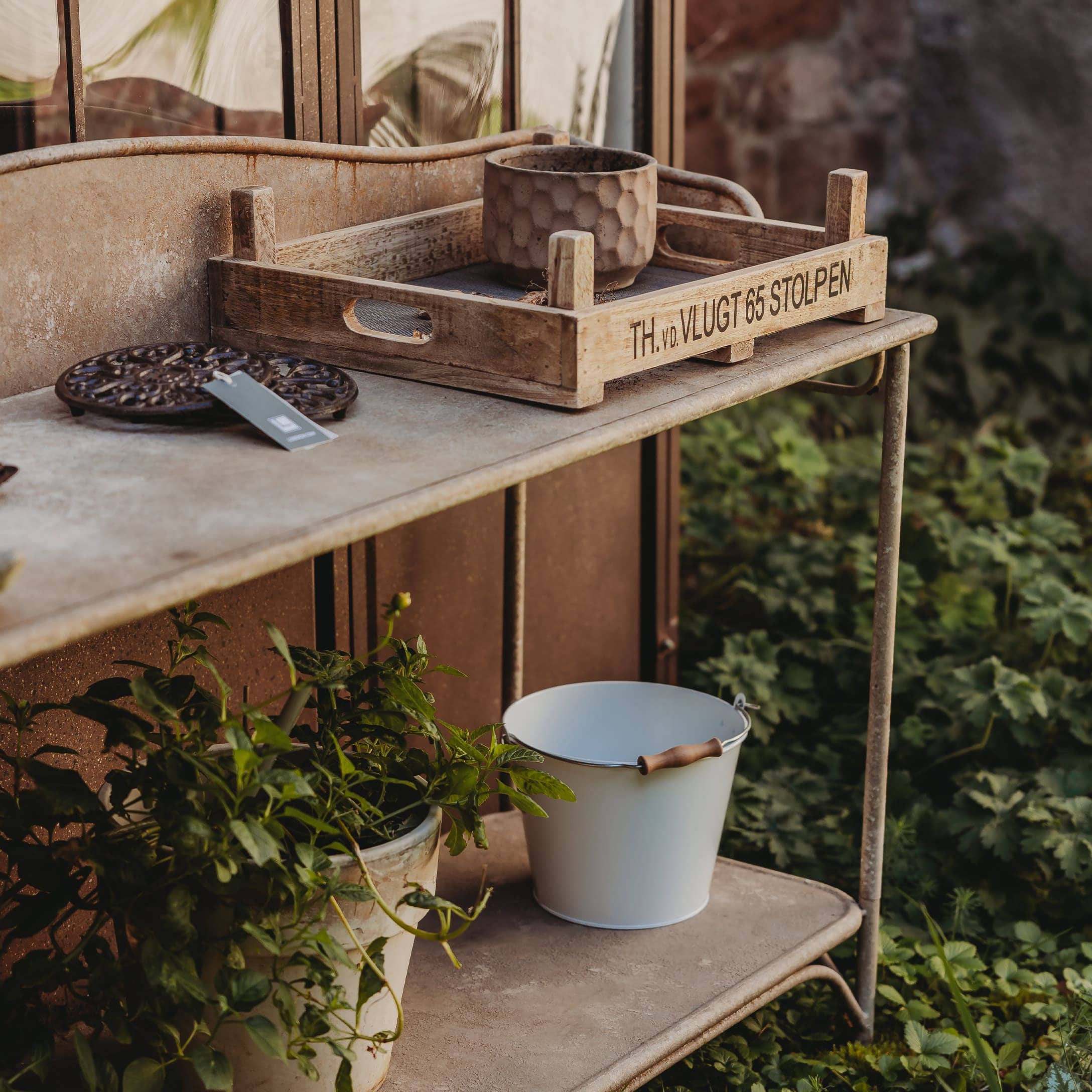Holztablett auf Metalltisch mit Blumentopf und weissem Eimer im Garten als Dekoration