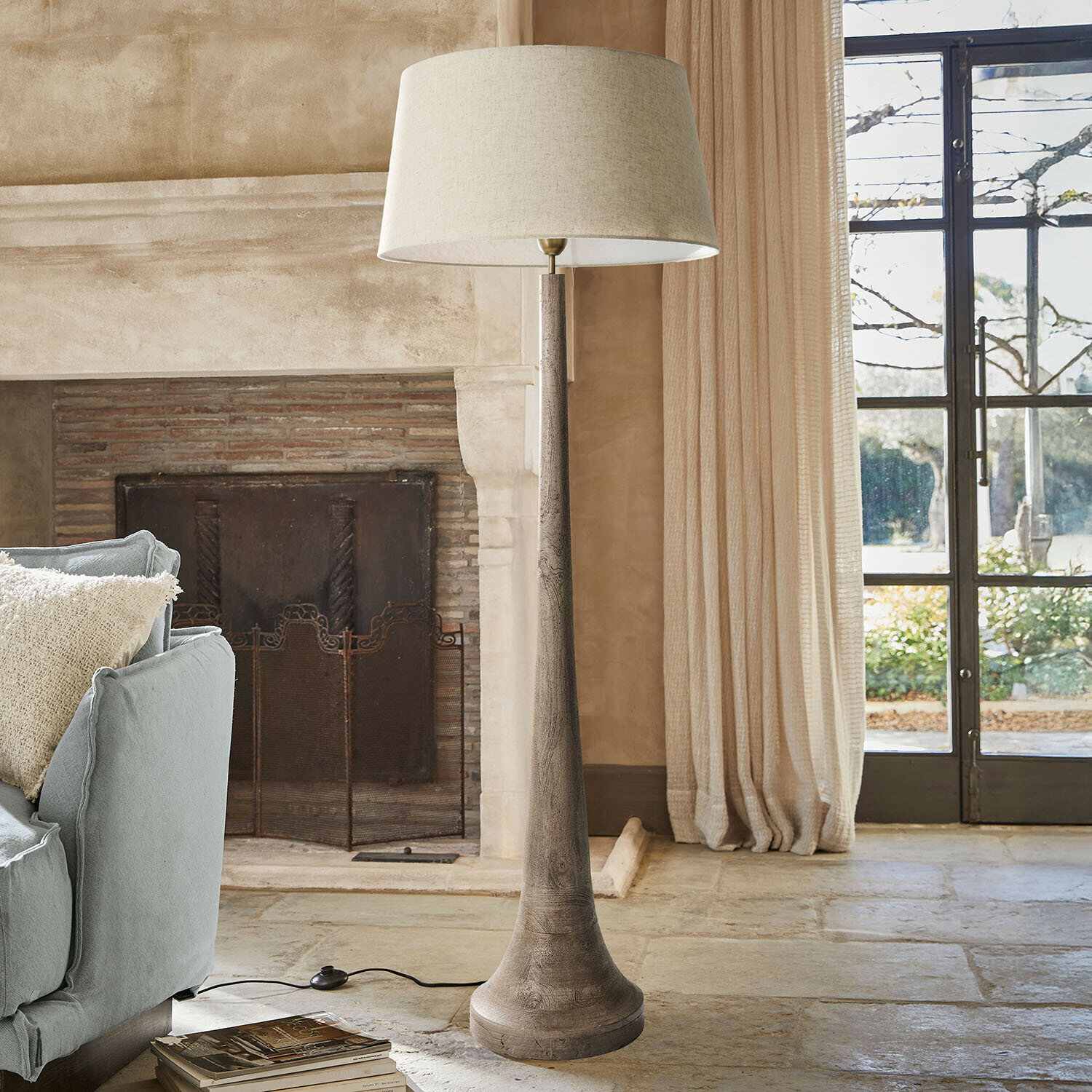 Stehlampe mit Holzsockel und beigem Lampenschirm in gemütlichem Wohnzimmer mit Cheminée