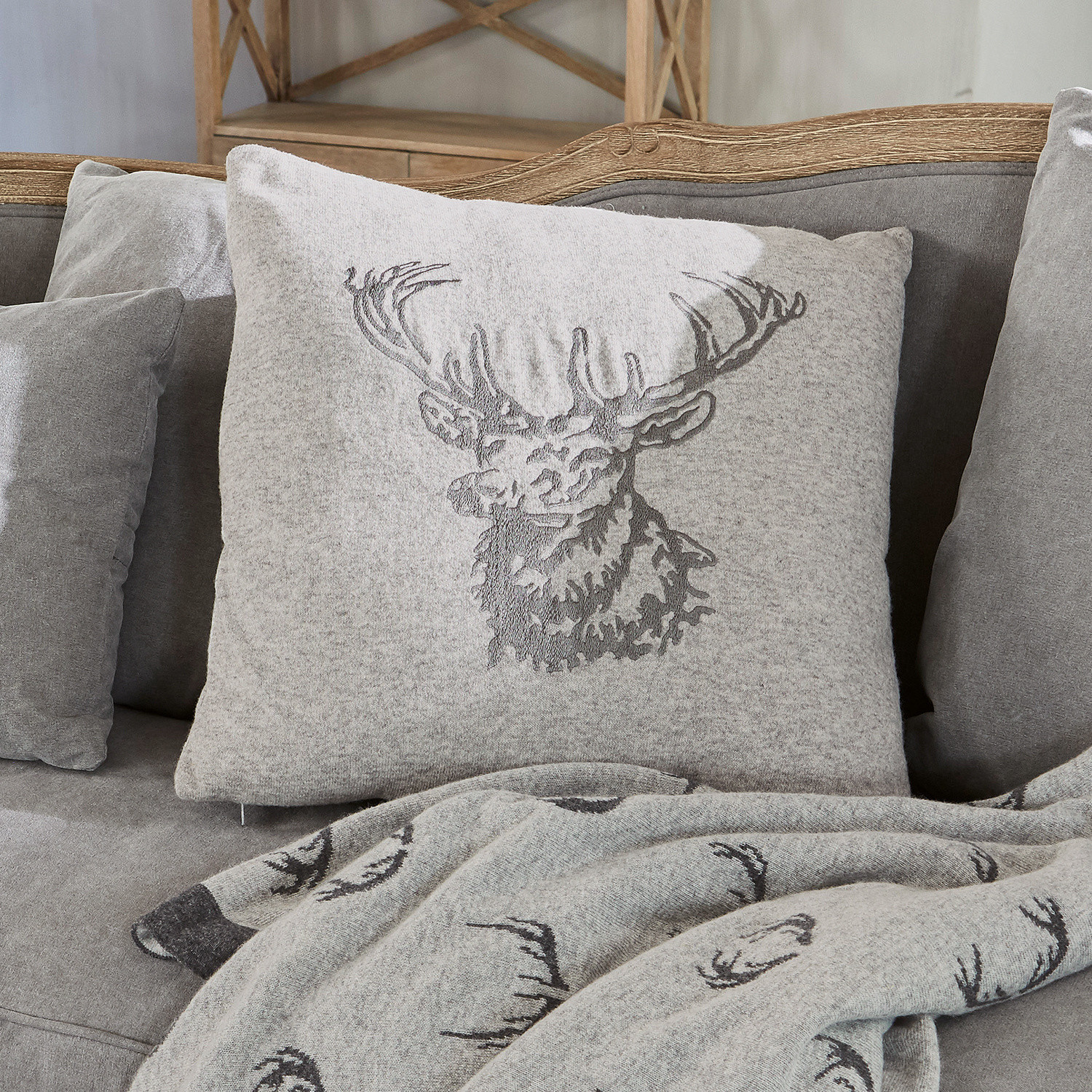 Kissenhülle Dario Graues Kissen aus weichem Material mit Hirschmotiv auf grauem Sofa mit passender Hirschdecke.