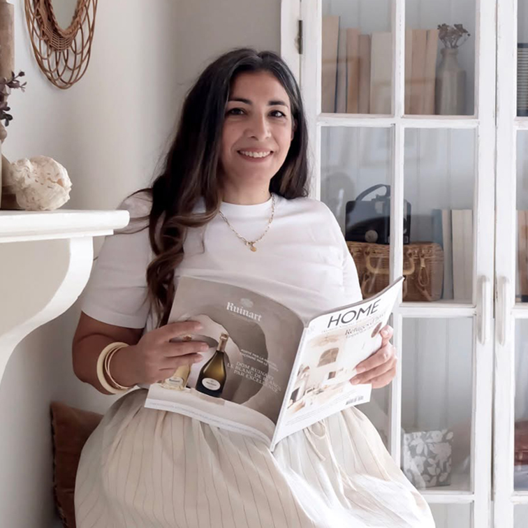 Frau in weissem Oberteil und hellem Rock liest Wohnmagazin in hellem Raum mit Holzschrank