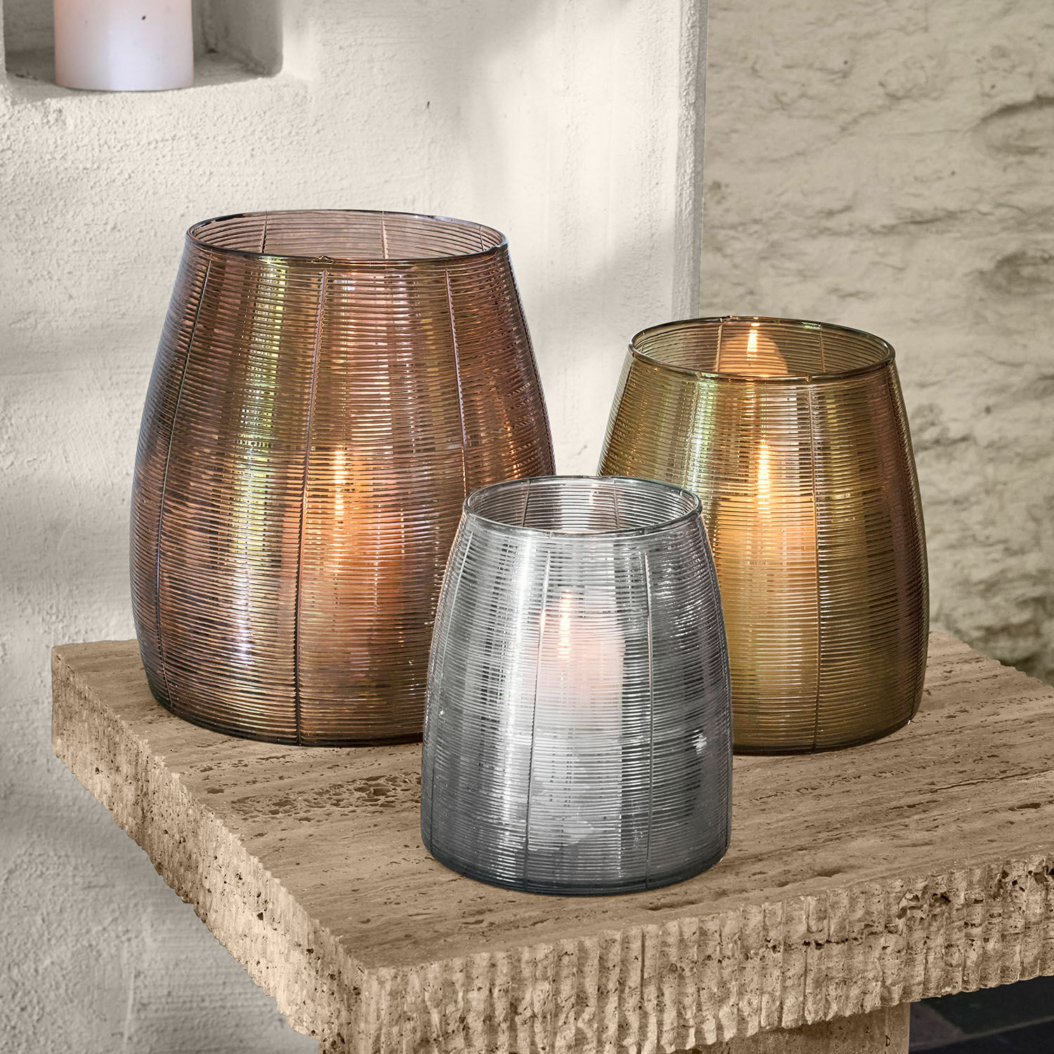 Windlicht 3er Set Uvenar Drei Glaslaternen in Bronze-, Gold- und Silberfarben auf einem Steintisch dekorativ arrangiert