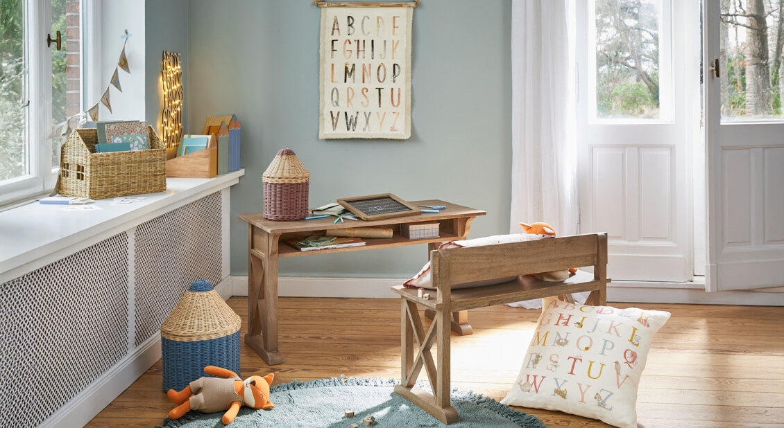 Kinderzimmer mit Holzschreibtisch und Bank, Kissen und Alphabet-Poster in sanften Pastellfarben