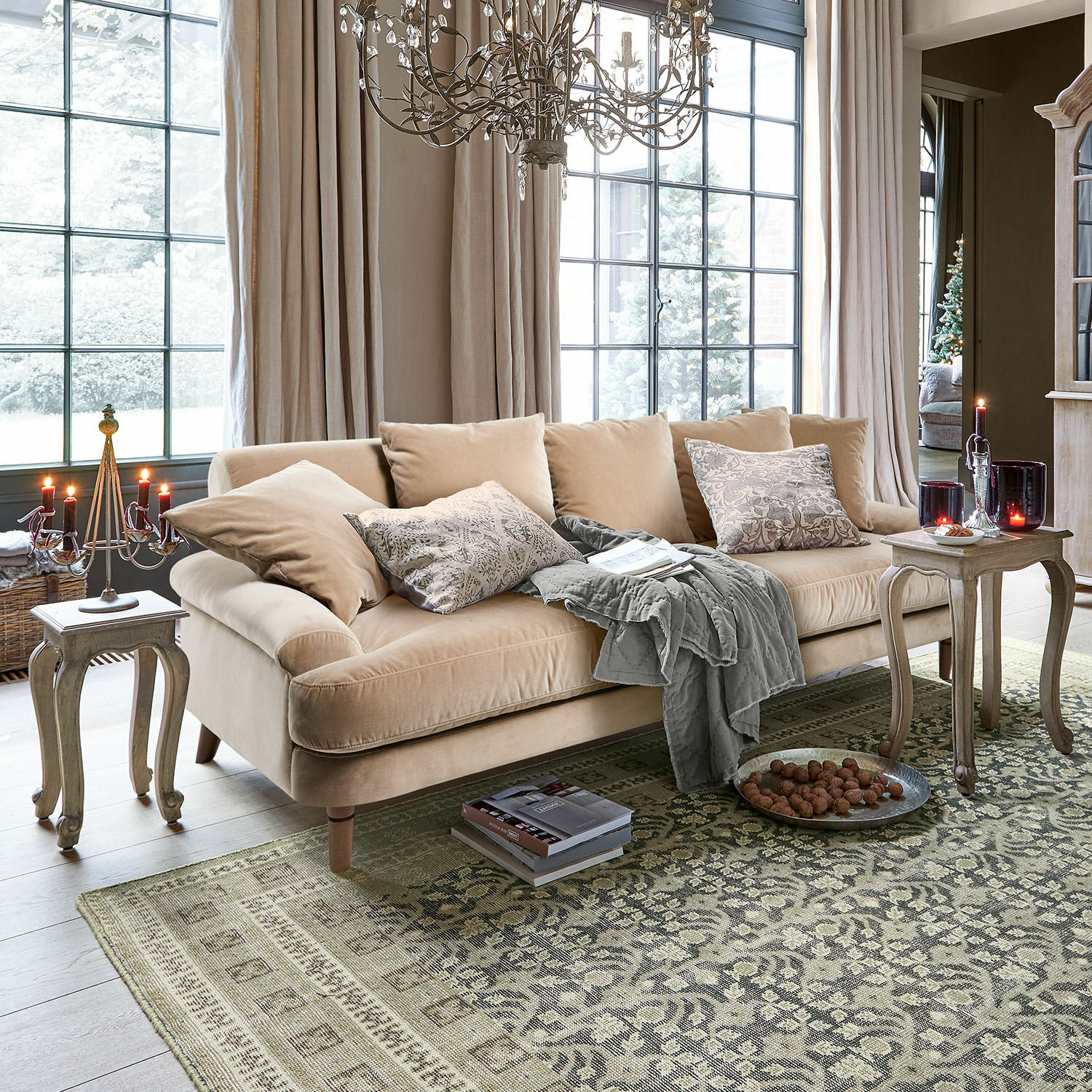 Sofa Rivermere Beiges Samtsofa mit Kissen und grauer Decke im hellen Wohnzimmer mit Teppich und Kerzen