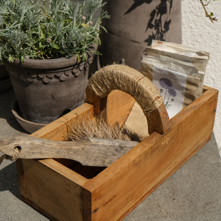 Holzkiste mit Griff aus Juteseil, gefüllt mit Bürste und Samenpäckchen, natürliche Materialien