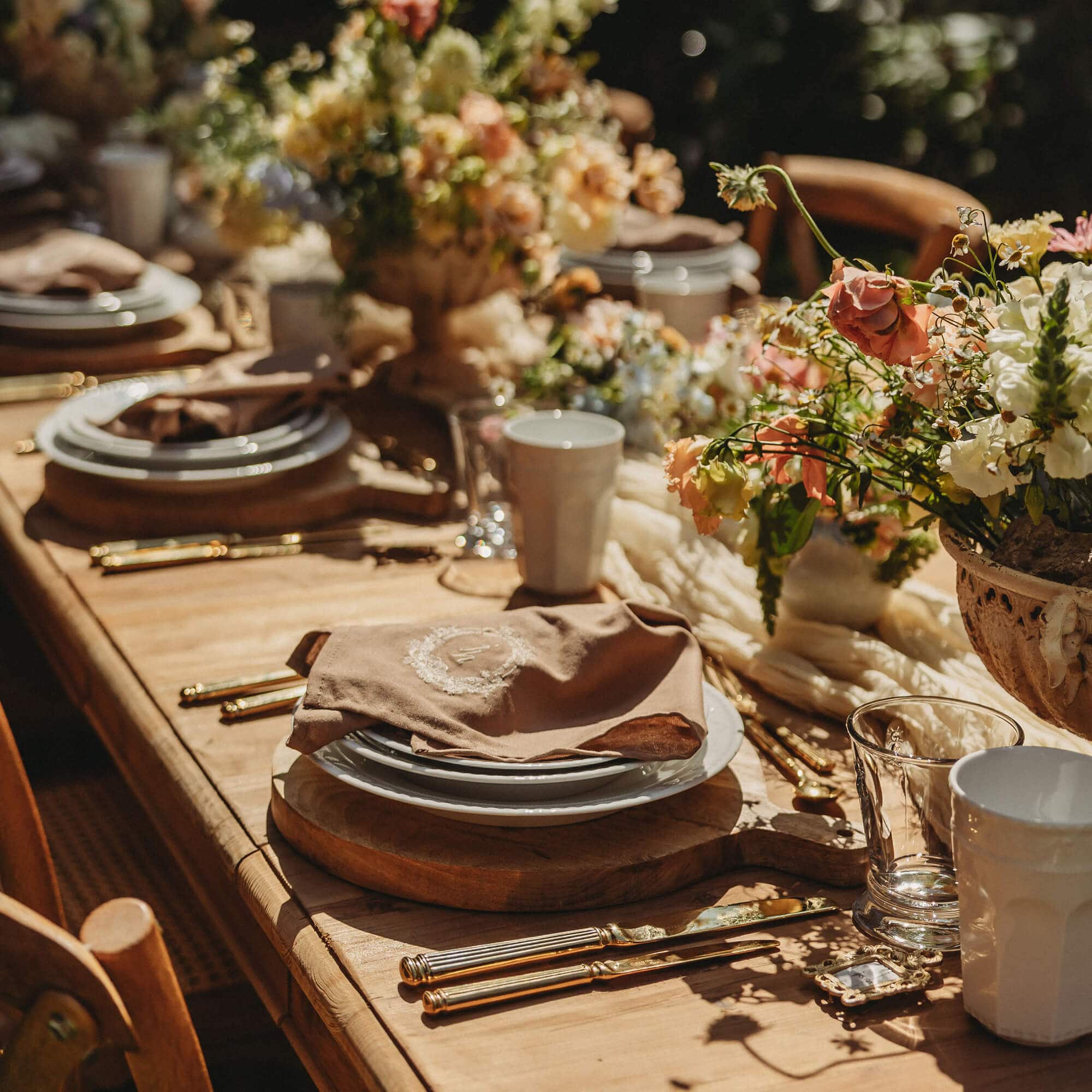 Rustikaler Holztisch mit Geschirr, goldenem Besteck und Blumenarrangement für festliches Essen