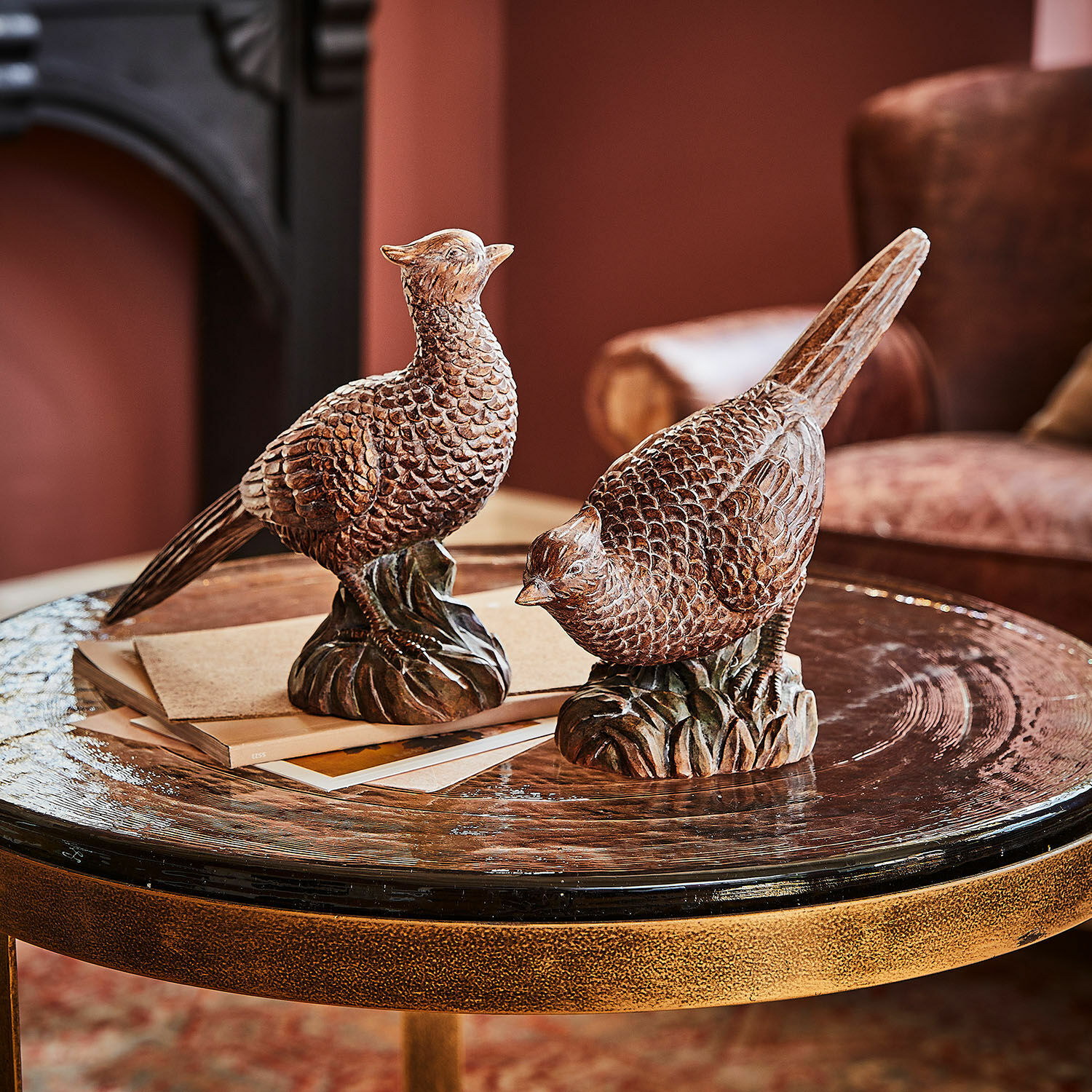 Deko-Vogel 2er Set Vivoso Zwei braune Holzvogel-Figuren auf einem Glastisch in einem gemütlichen Wohnzimmer