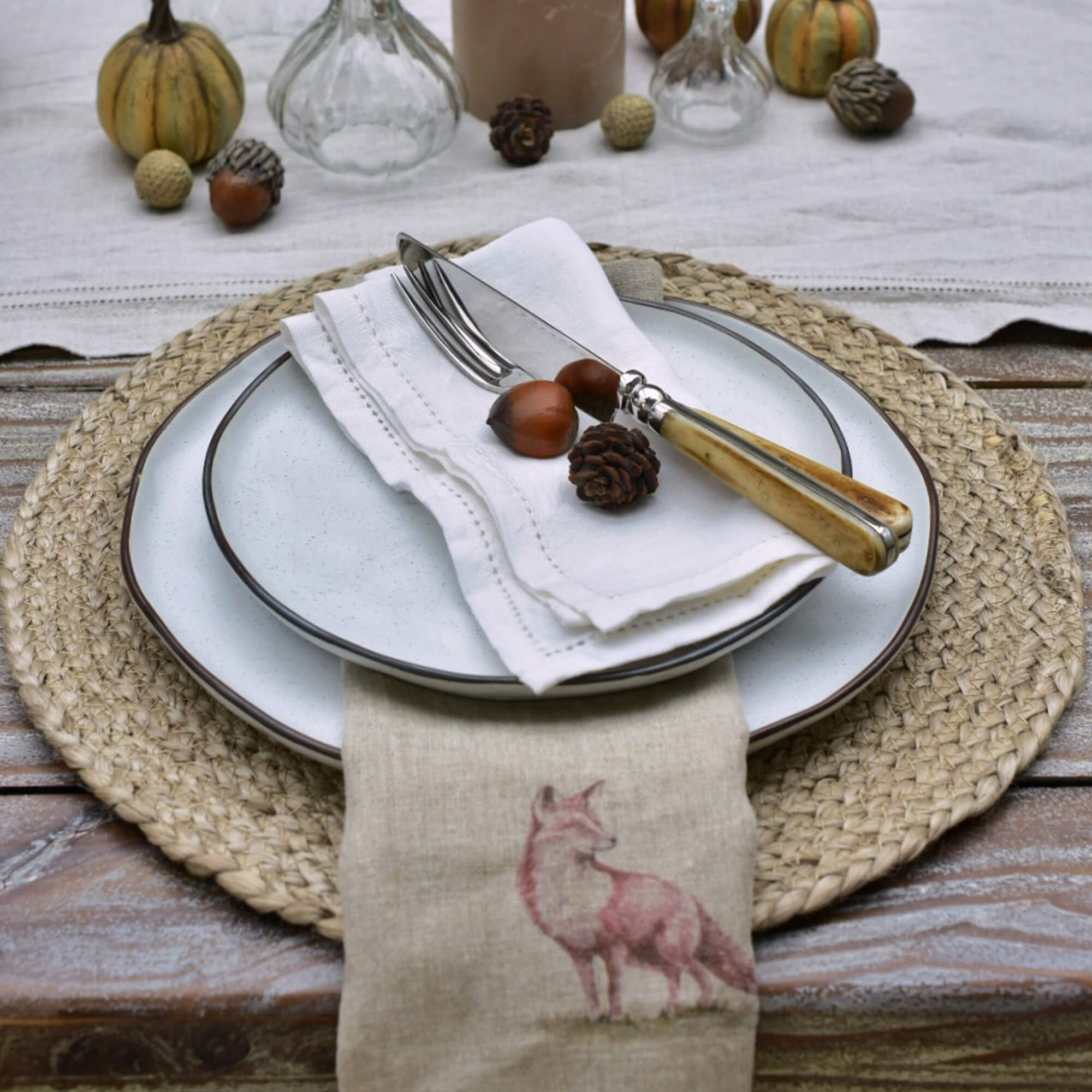 Tischservice mit weissen Keramiktellern, Besteck mit hellem Holzgriff und Leinenserviette mit Fuchsmotiv