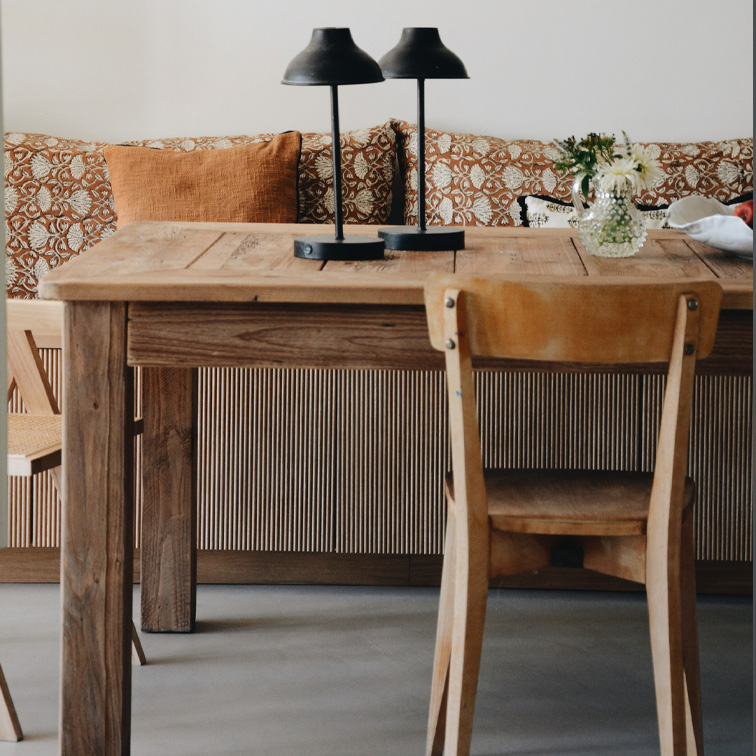 Holztisch mit zwei schwarzen Lampen und Blumen in Vase vor Sofa mit orangefarbenen Kissen