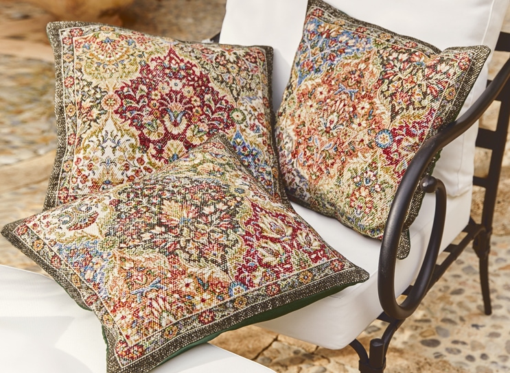 Drei dekorative Kissen mit orientalischem Muster in warmen Farben auf weissem Metallstuhl