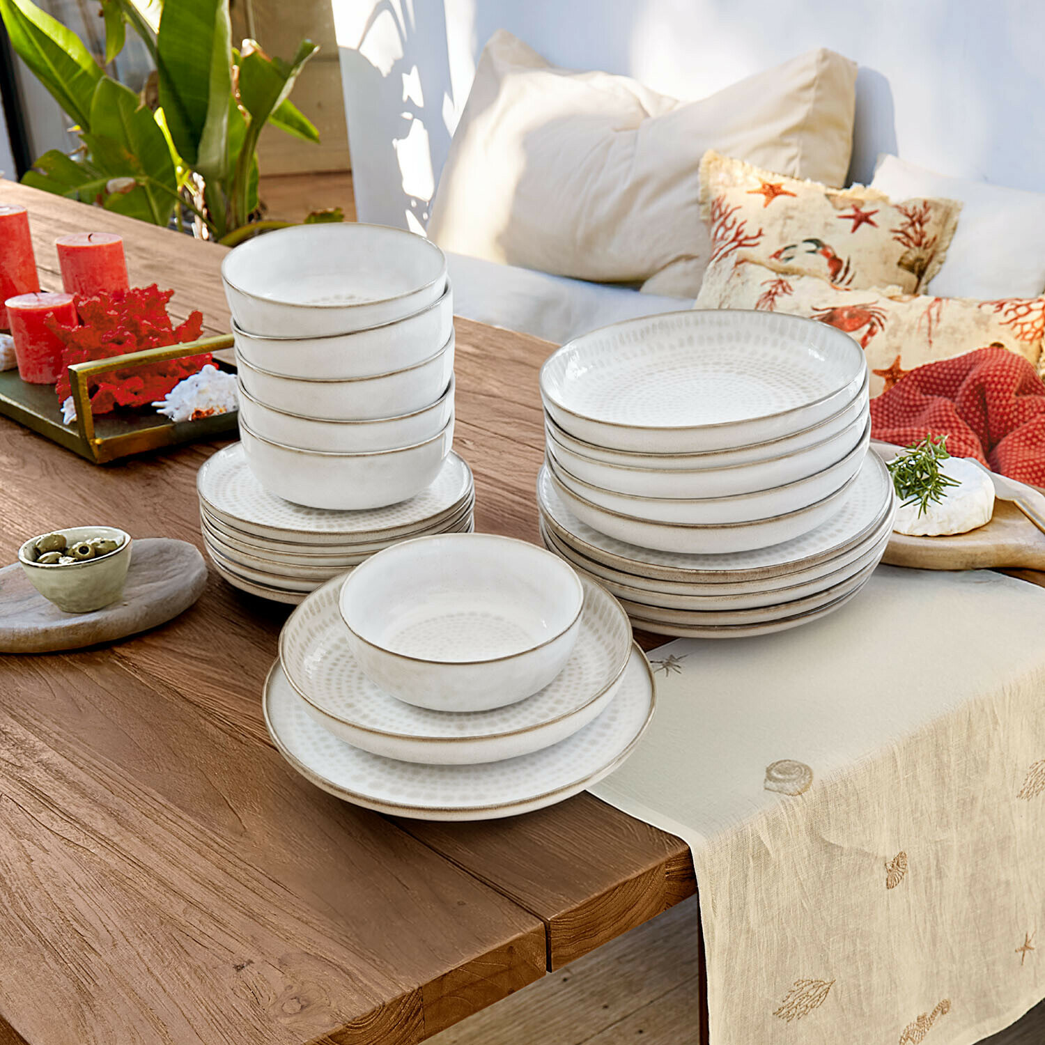 Weisses Keramik-Geschirrset mit Tellern und Schalen auf Holztisch mit Dekoration