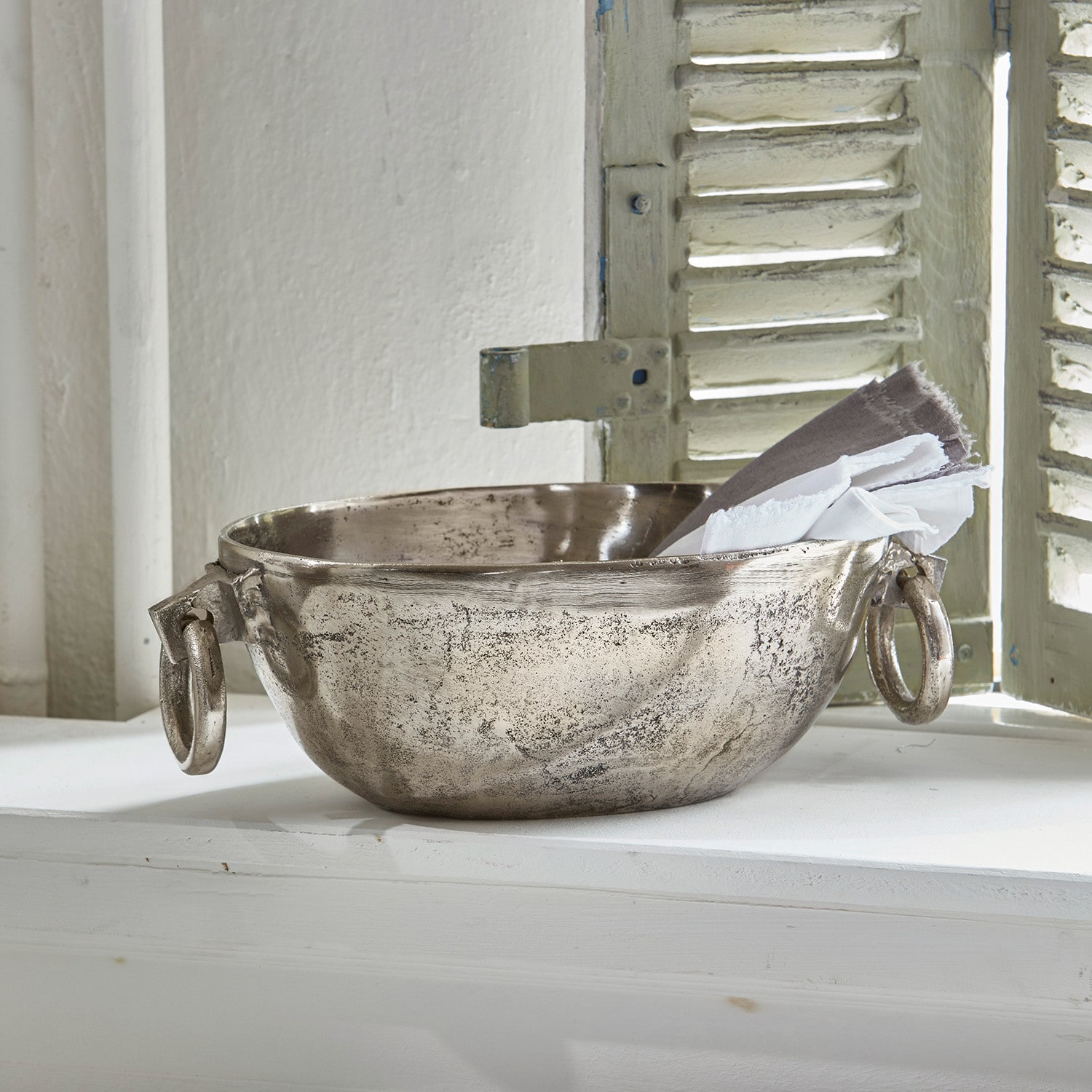 Dekorative Metallschale in Silber mit Griffen und Leinentüchern auf der Fensterbank