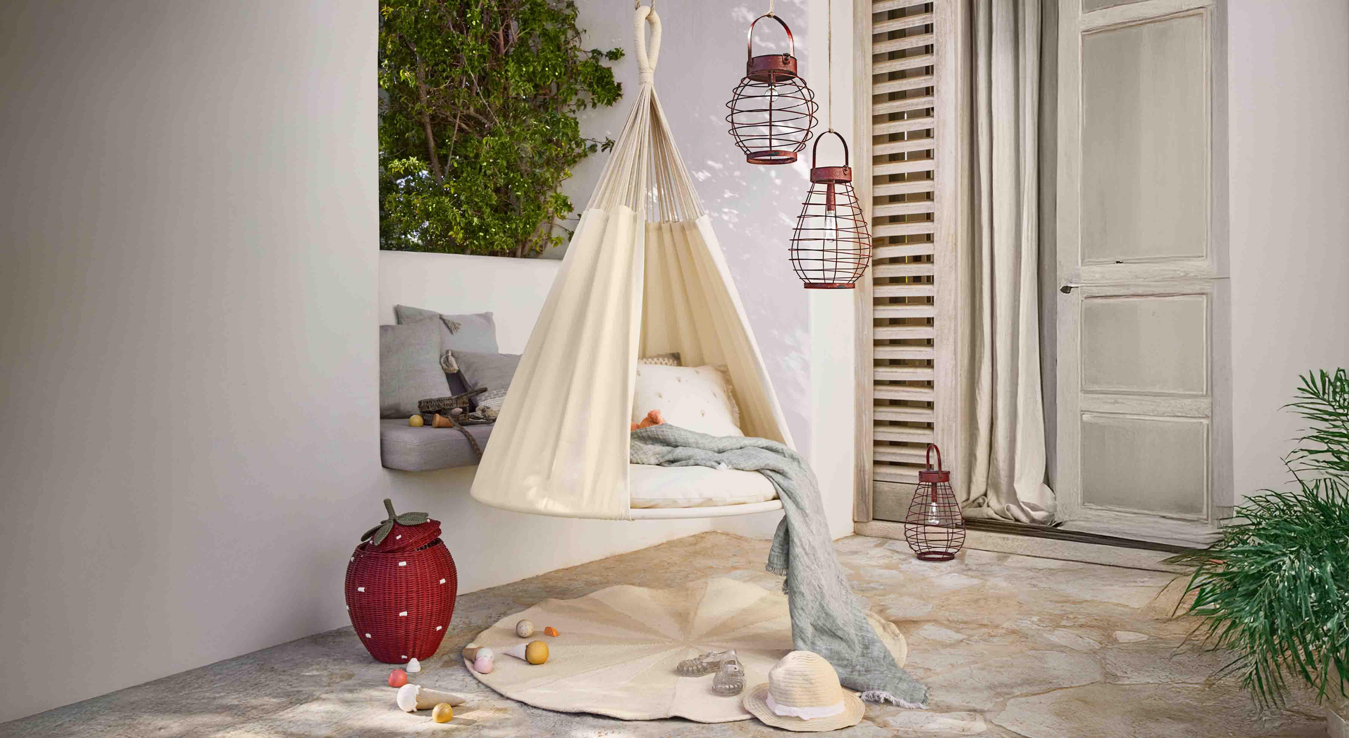 Beiger hängender Stoffsessel auf Terrasse mit Kissen und dekorativen Metalllaternen