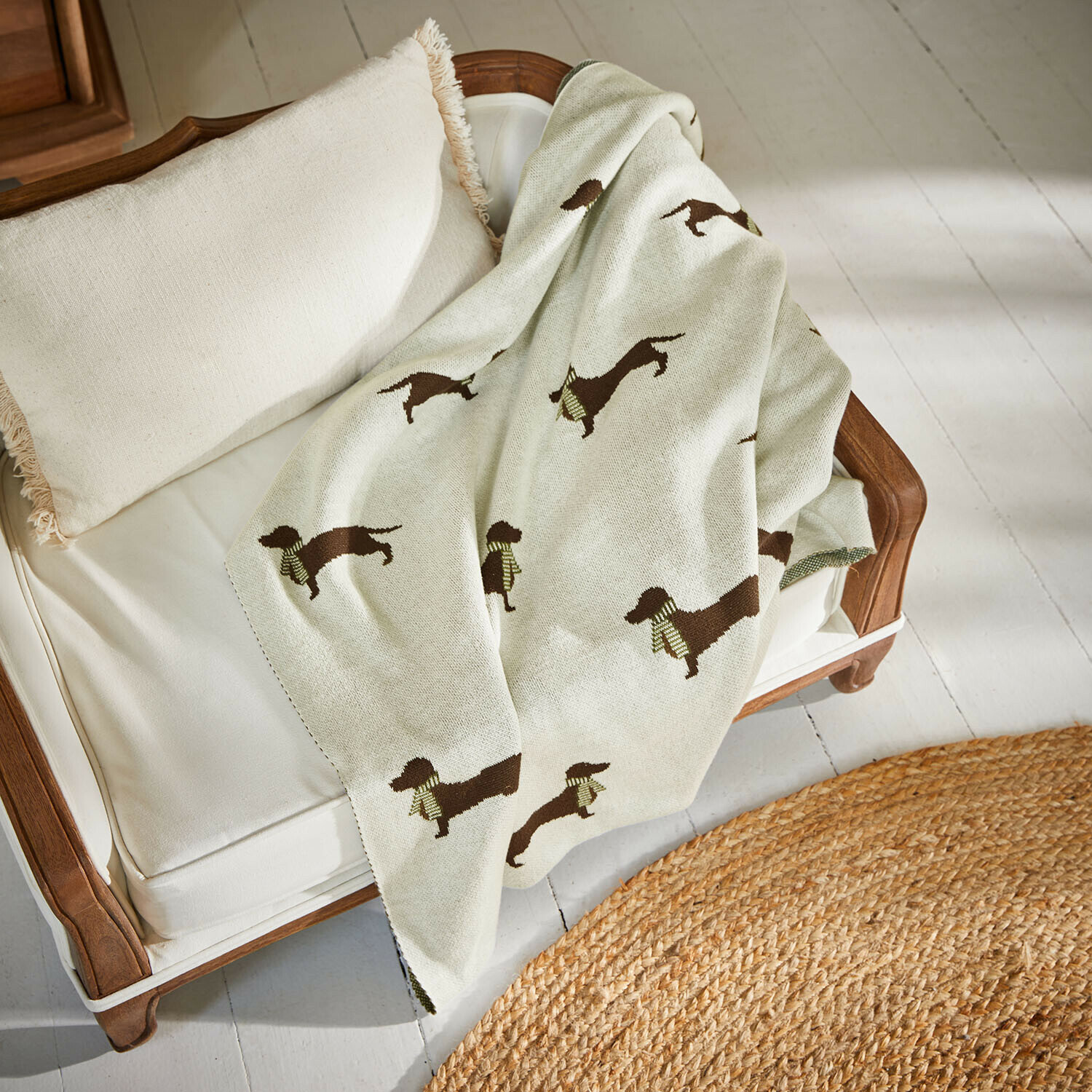 Hundedecke Brisette Beige Decke mit Dackel-Motiv auf weissem Sofa mit Holzrahmen und Kissen mit Fransen