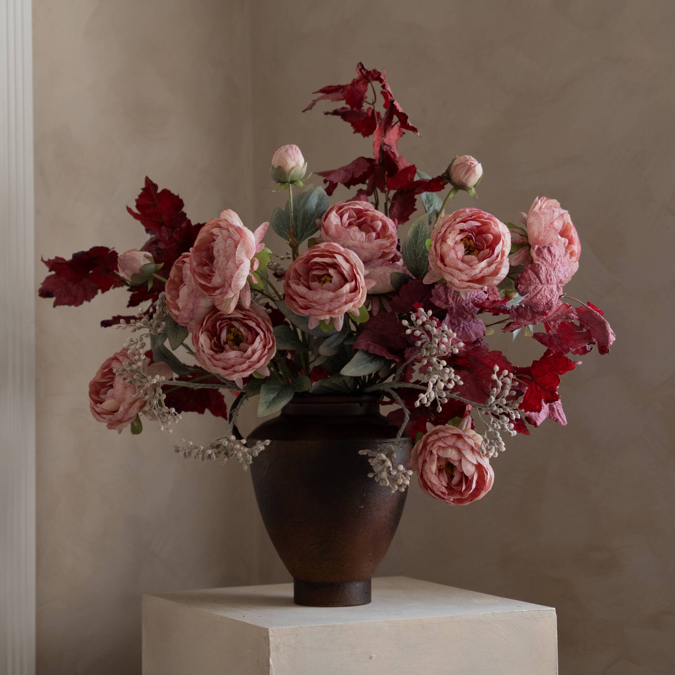 Strauß mit rosa Rosen und roten Blättern in dunkler Keramikvase auf hellem Sockel