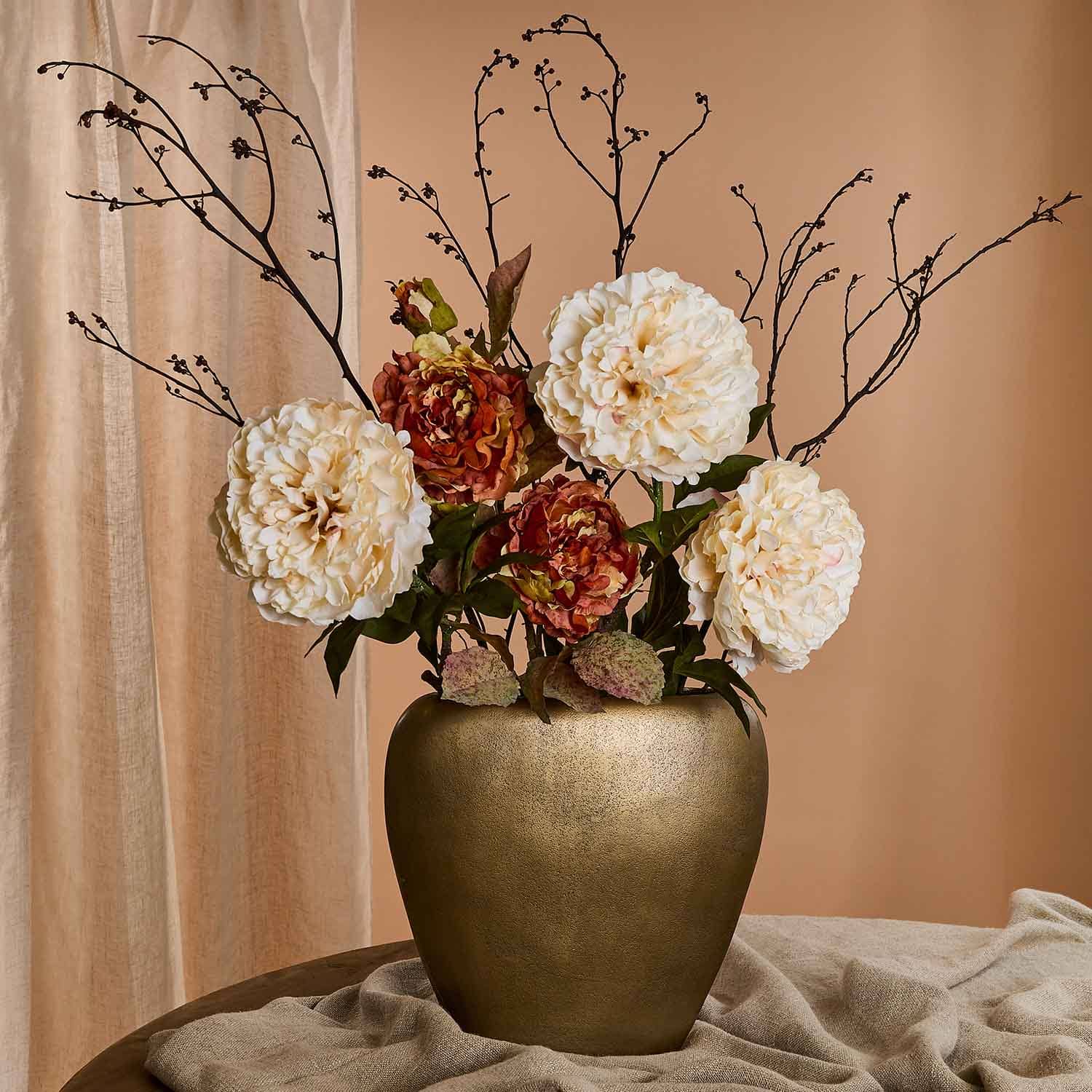 Strauß aus cremefarbenen und braunen Blumen in goldener Keramikvase vor beigem Hintergrund