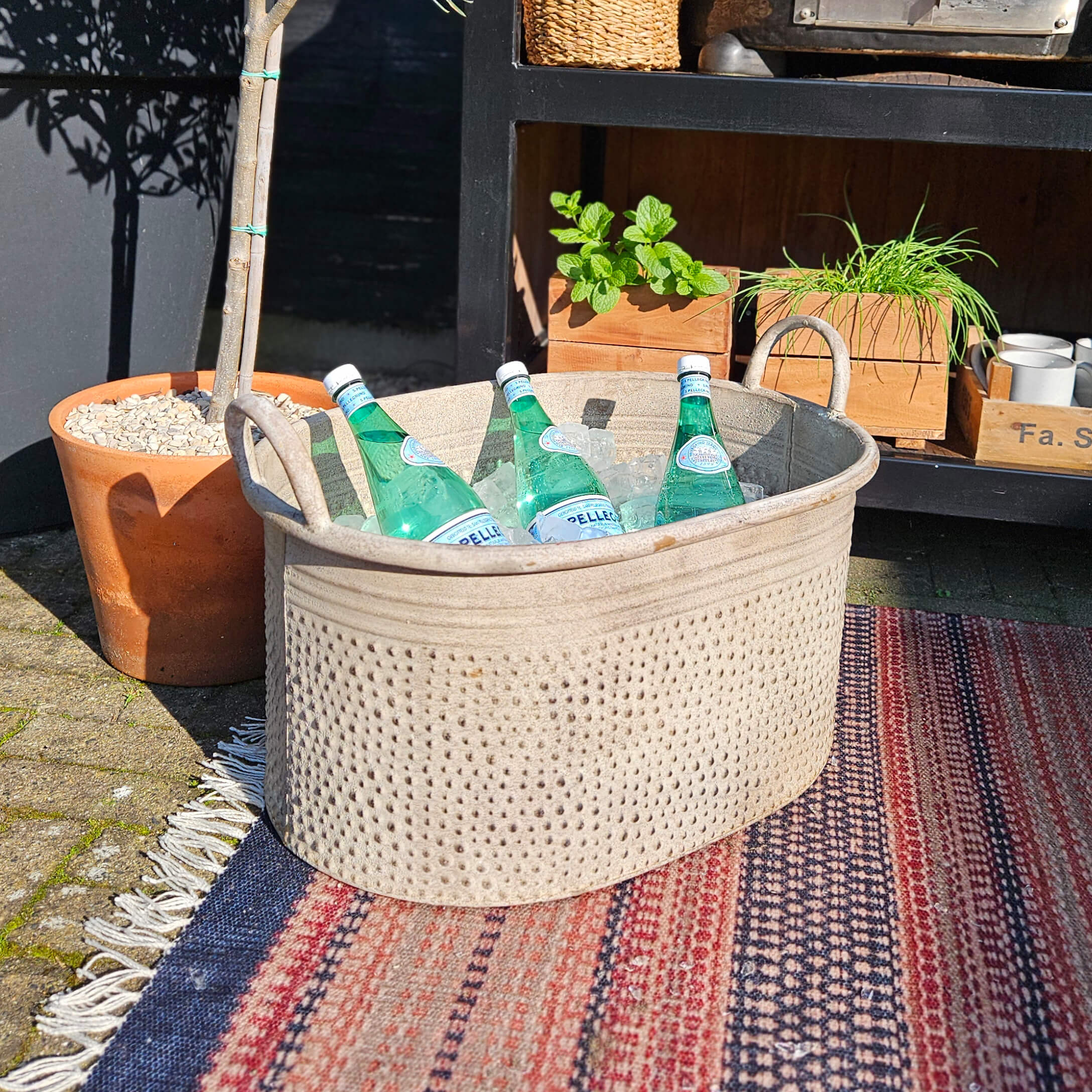 Beiger Stoffkorb mit Griffen, gefüllt mit Mineralwasserflaschen auf Eis, draussen auf Teppich