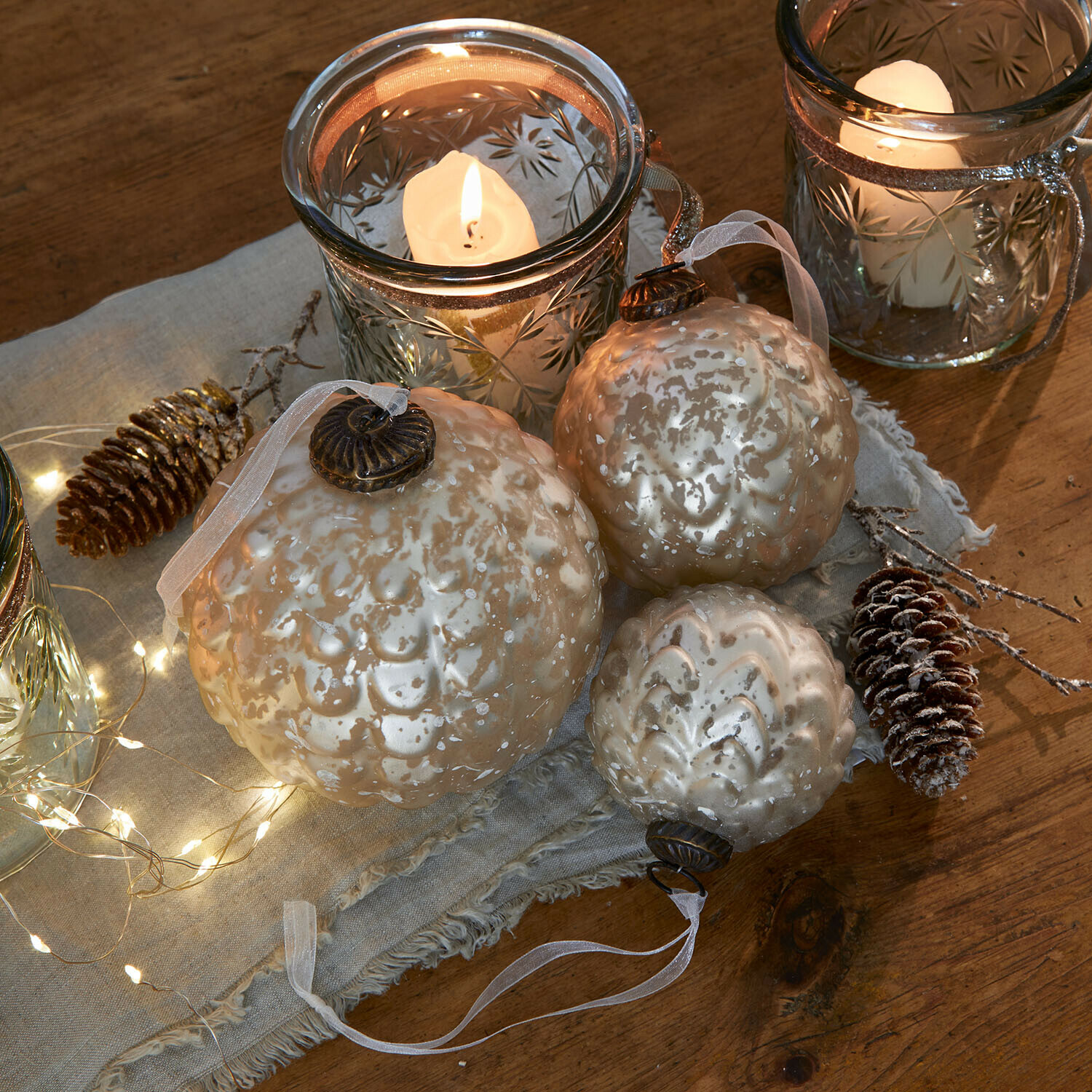 Weihnachtskugel 6er Set Domara Set mit drei perlmuttfarbenen Glas-Weihnachtskugeln mit dekorativem Muster und Kerzenlicht im Hintergrund